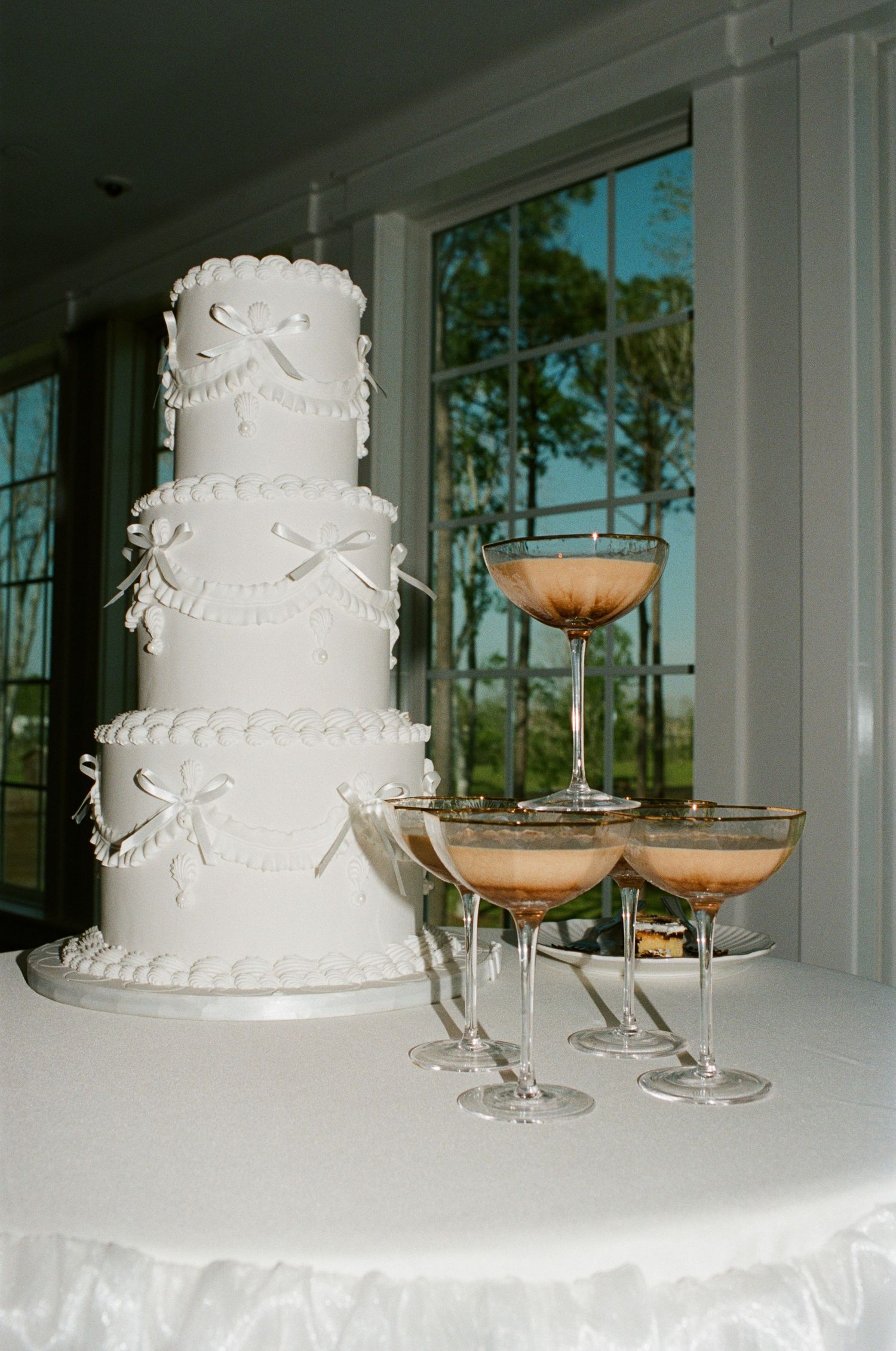 Elegant white wedding cake with delicate decorations displayed next to champagne glasses.