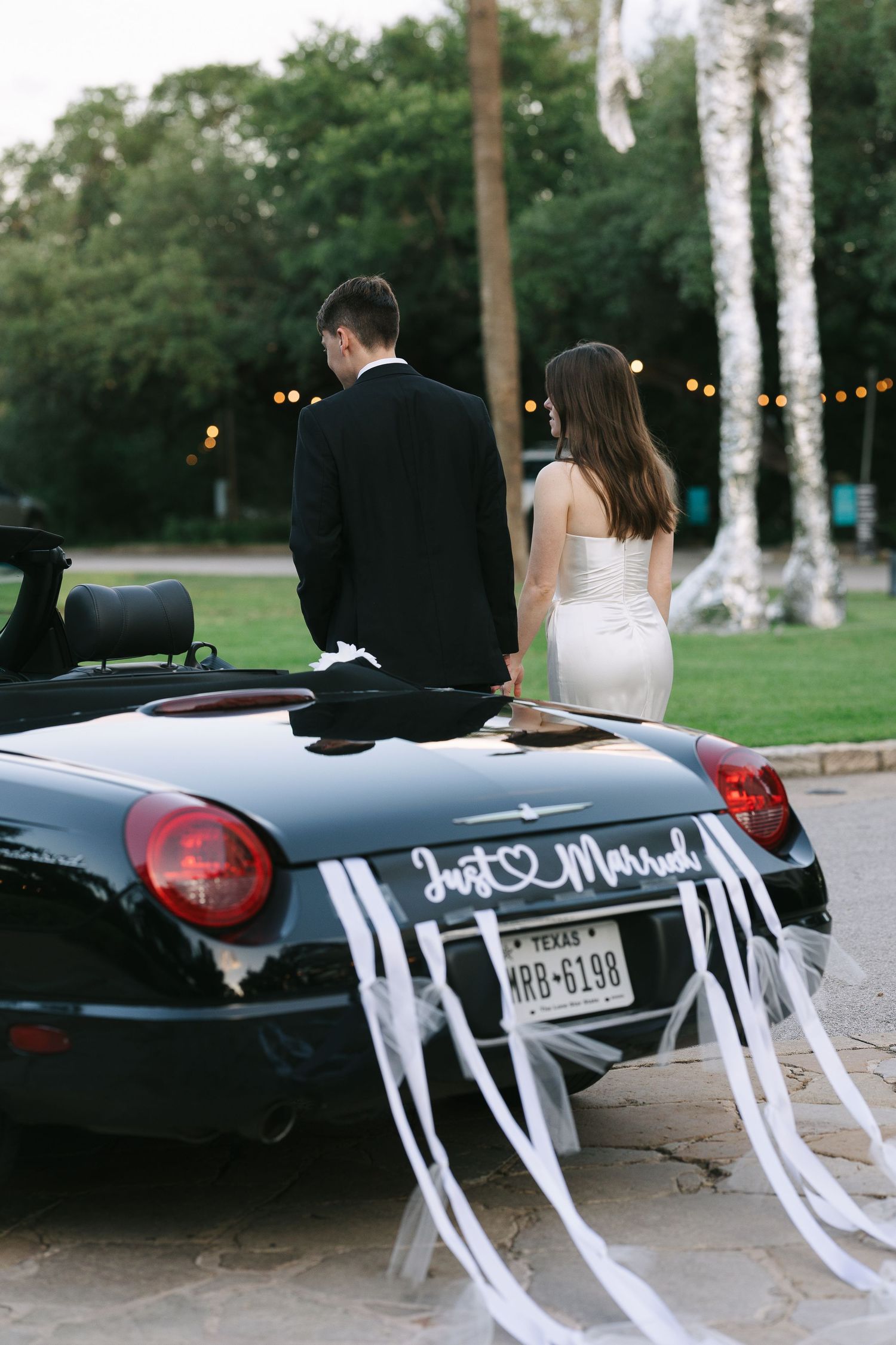 Black convertible car decorated with white streamers for a wedding.