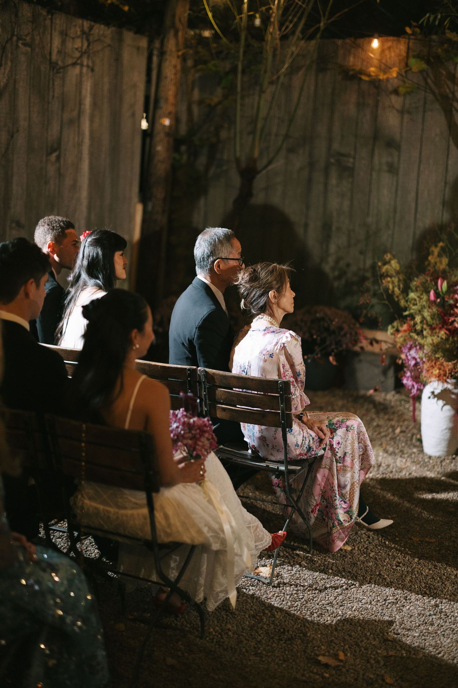Guests relax on benches during an outdoor evening wedding reception.