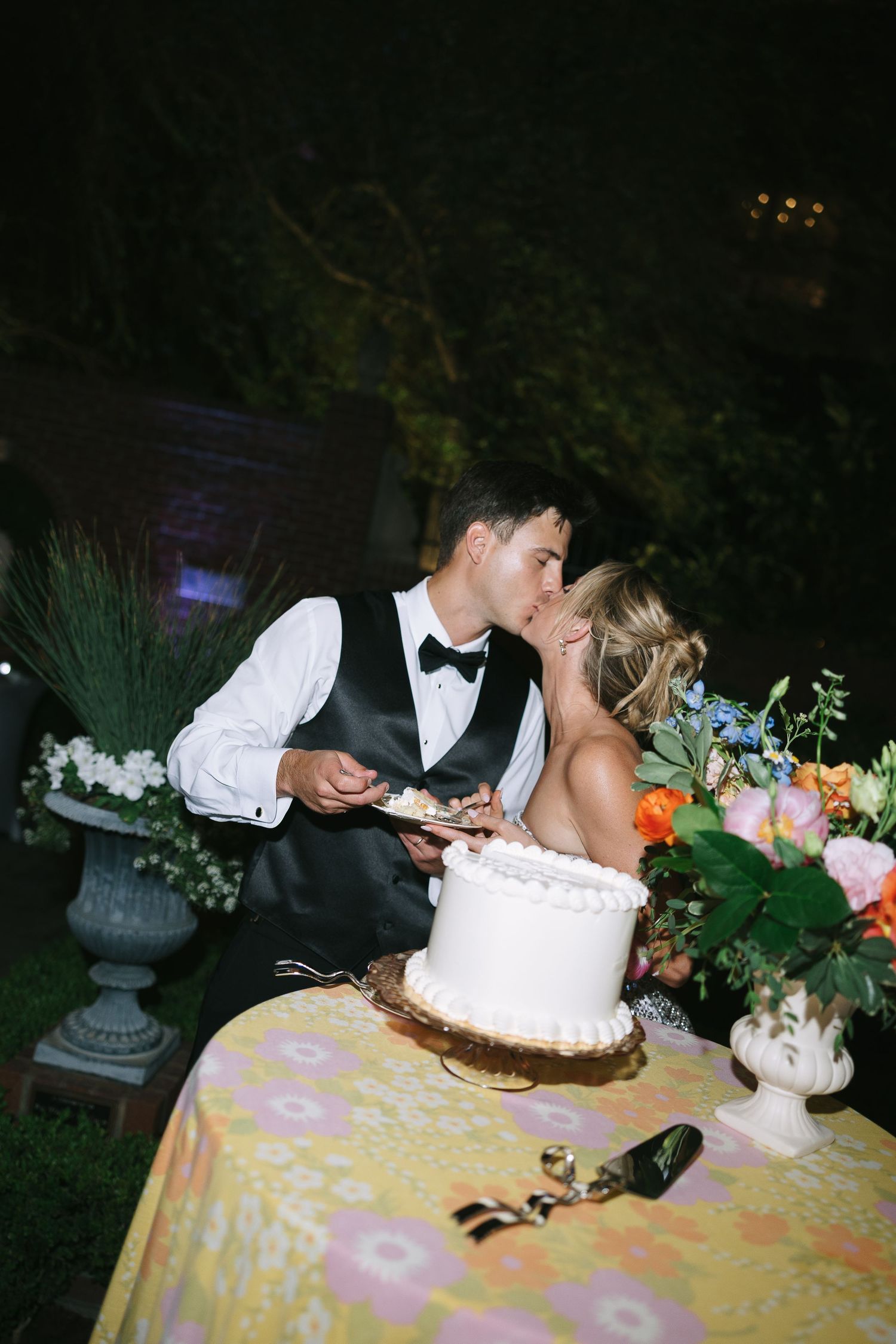 Wedding couple leaning in close while cutting their tiered white cake.