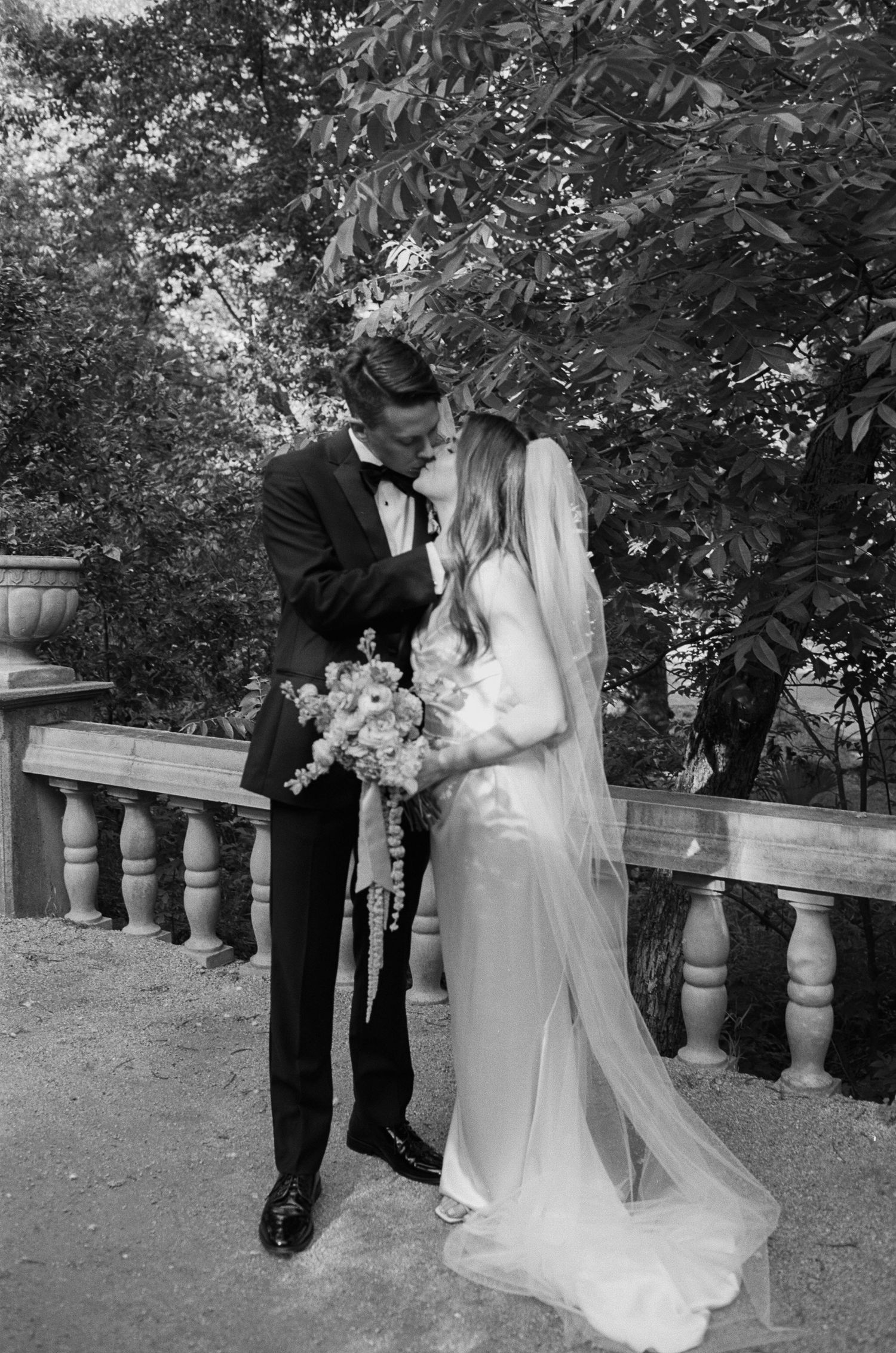 Black and white wedding photos captured on a garden terrace with stone railings.