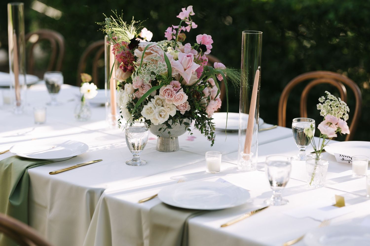 Elegant table settings with delicate floral arrangements and copper accents at an outdoor reception.