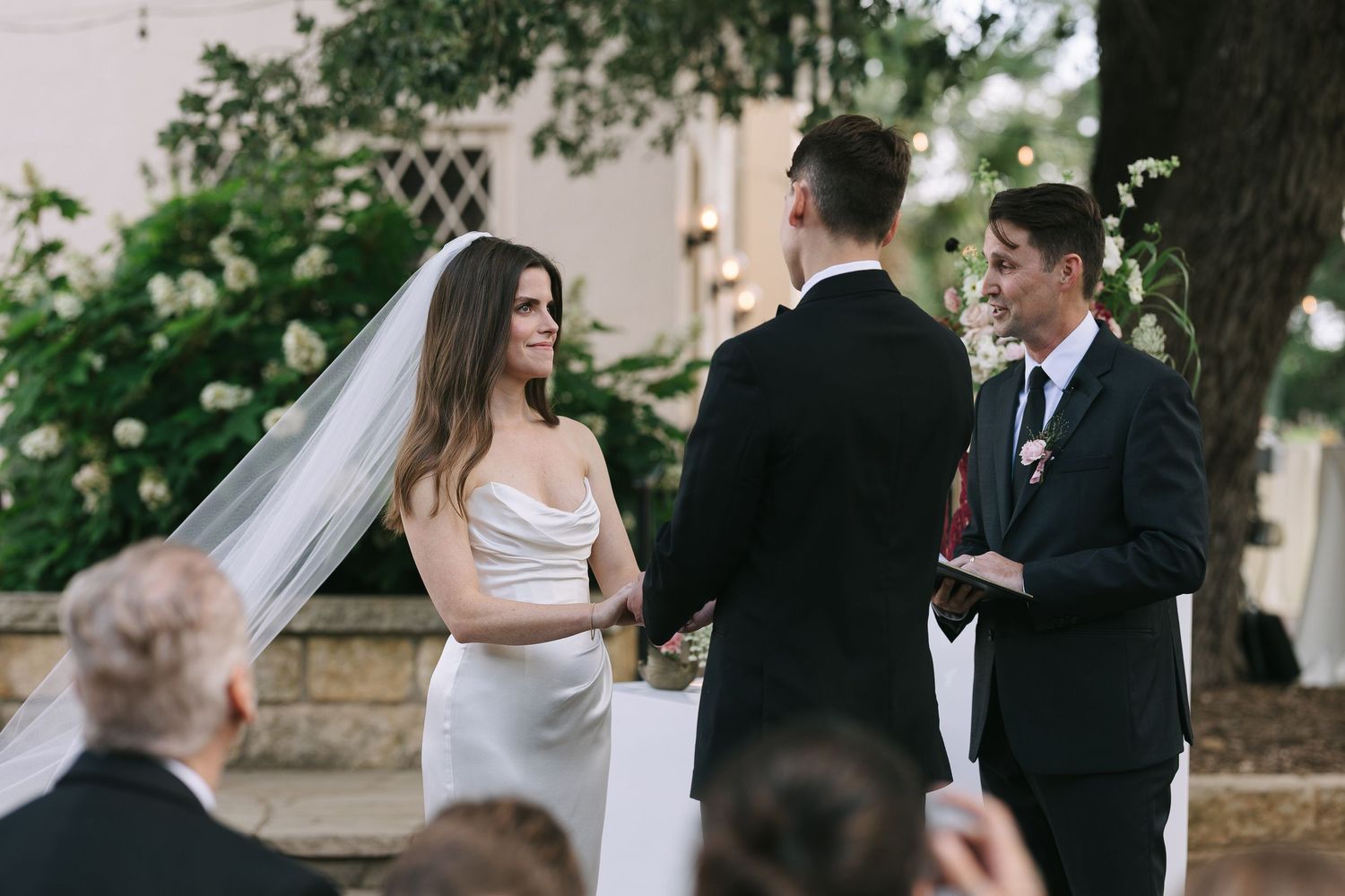 Wedding ceremony taking place outside historic building with white columns and windows.
