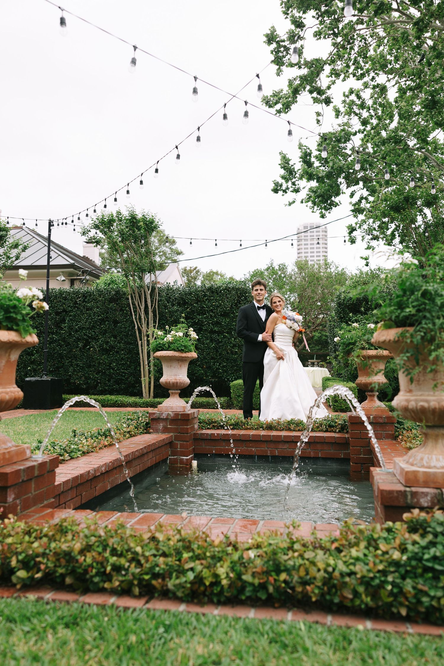 Garden wedding venue with string lights and water features surrounded by greenery.