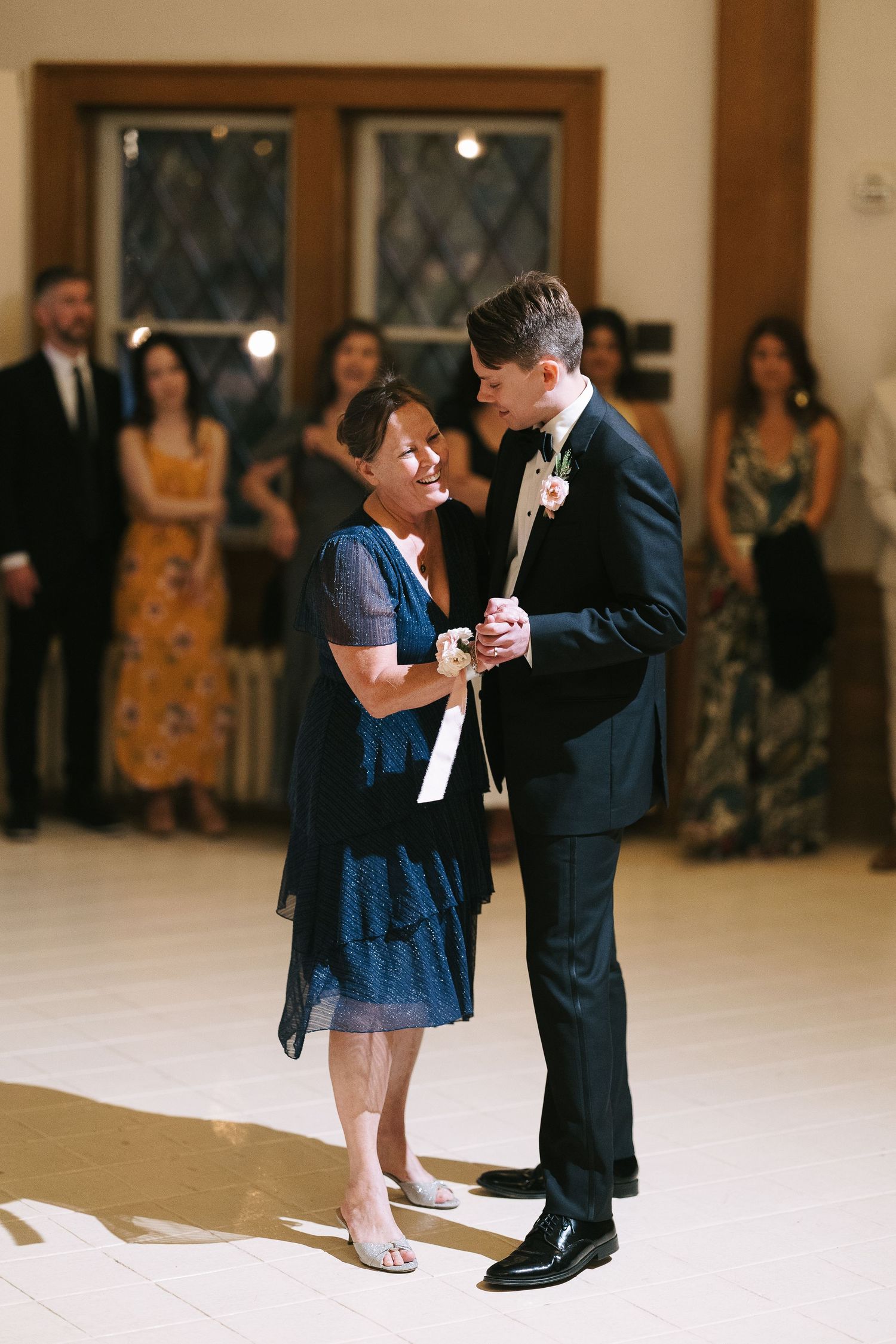 A young child in a navy dress dances with someone in a suit at a formal event.