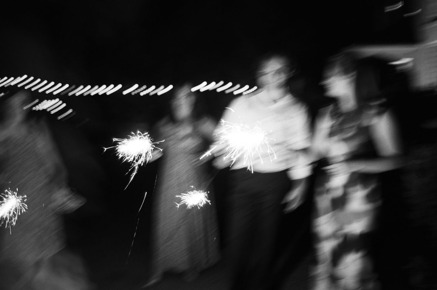 Blurred motion photograph of wedding guests holding sparklers creating light trails in the dark.