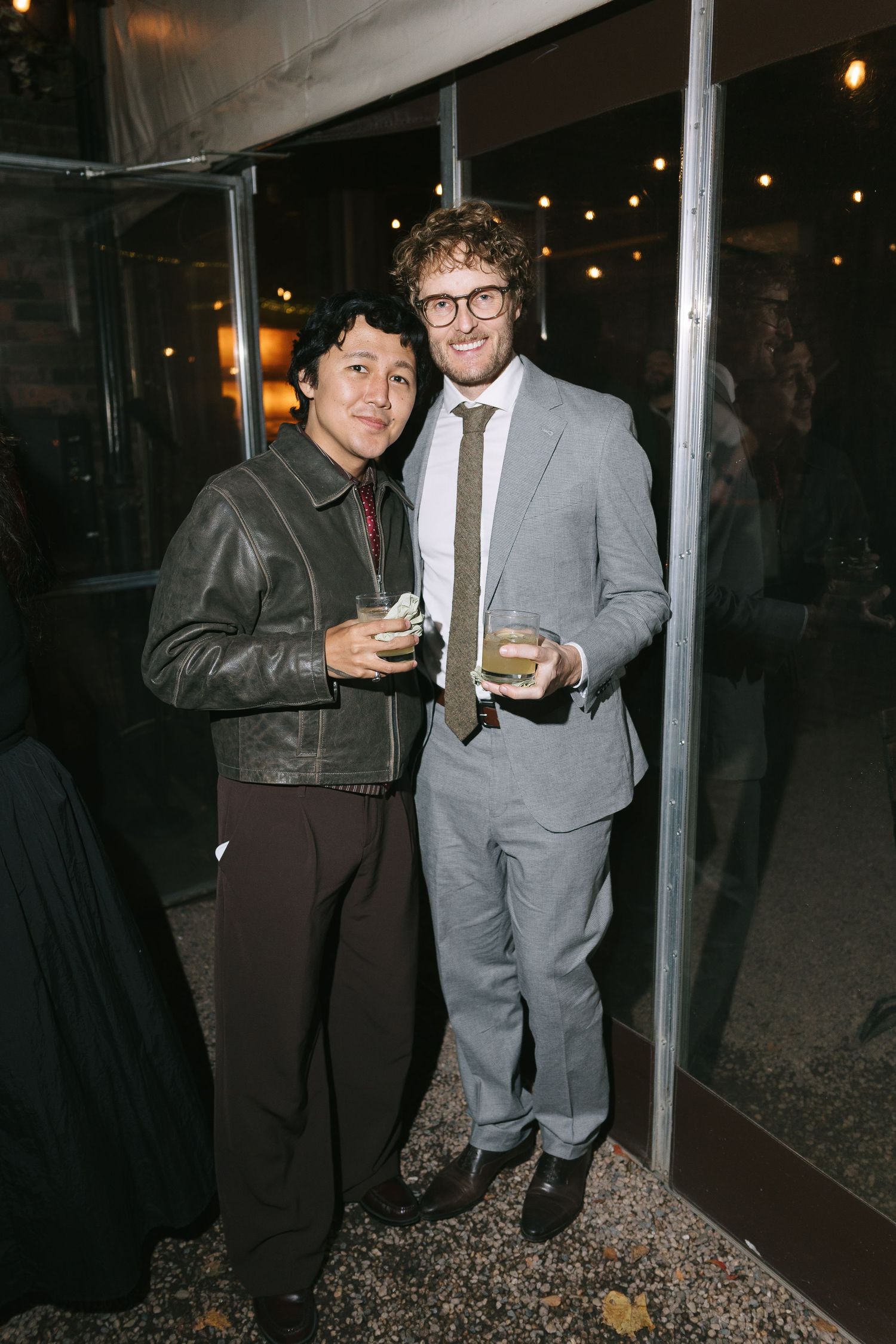 Two guests sharing a moment and drinks by metal poles at an indoor venue.