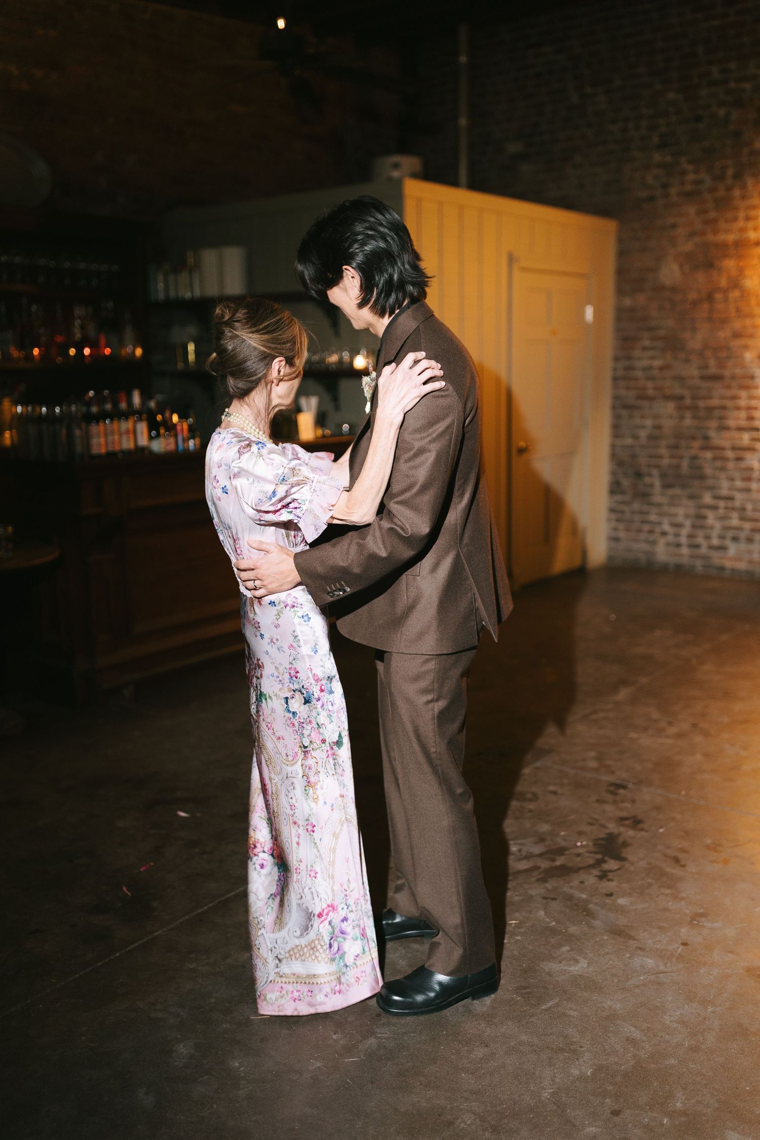 A couple shares an intimate dance together in a dimly lit brick-walled space.