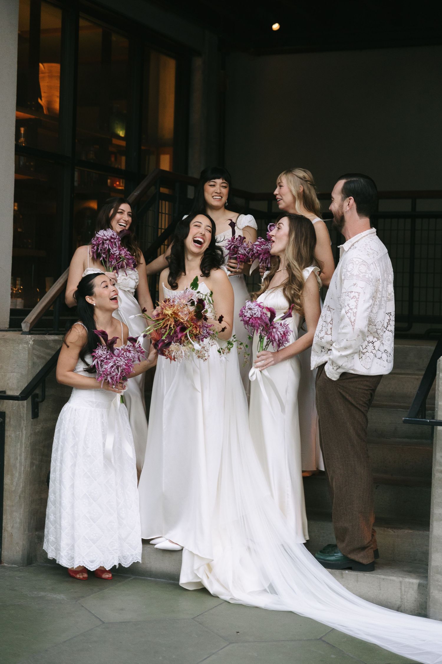 Wedding party shares joyful moments together while holding bright purple flower bouquets.