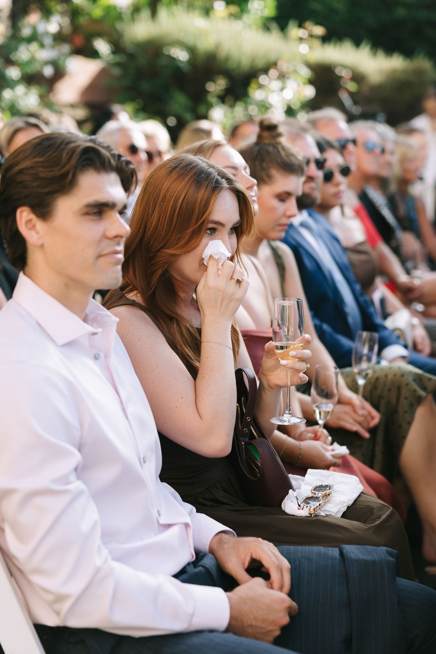 Wedding guests seated outdoors watching emotional ceremony.