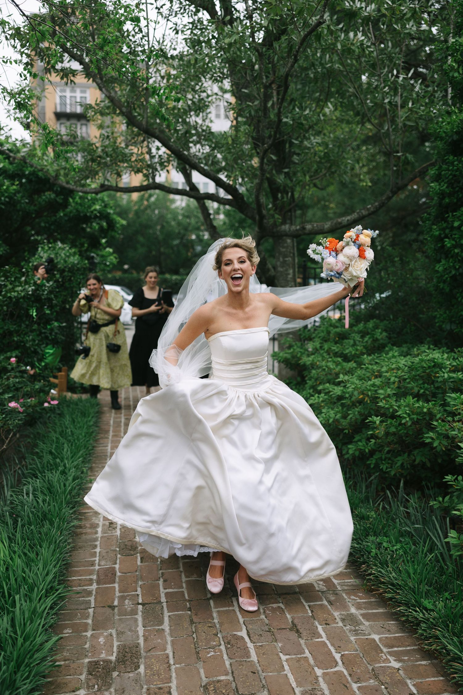 Wedding celebration on a brick pathway with joyful movements and flowing white dress.