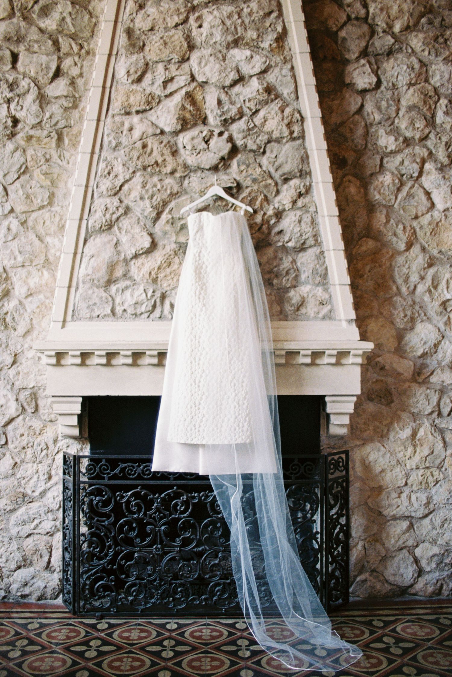 White lace wedding dress and veil hanging on stone fireplace mantel.