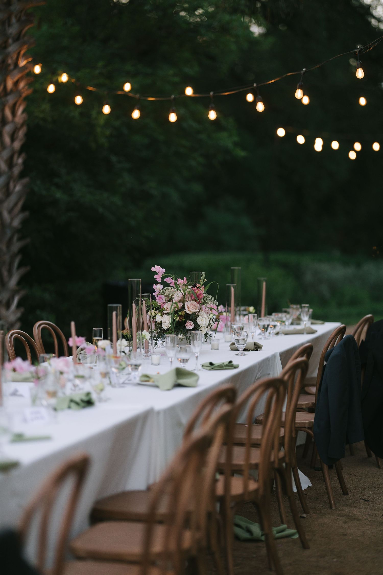 An elegant outdoor dining table set with string lights and floral centerpieces.