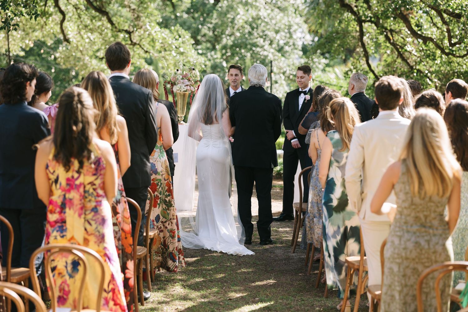 Outdoor wedding ceremony guests standing in a garden setting with string lights overhead.