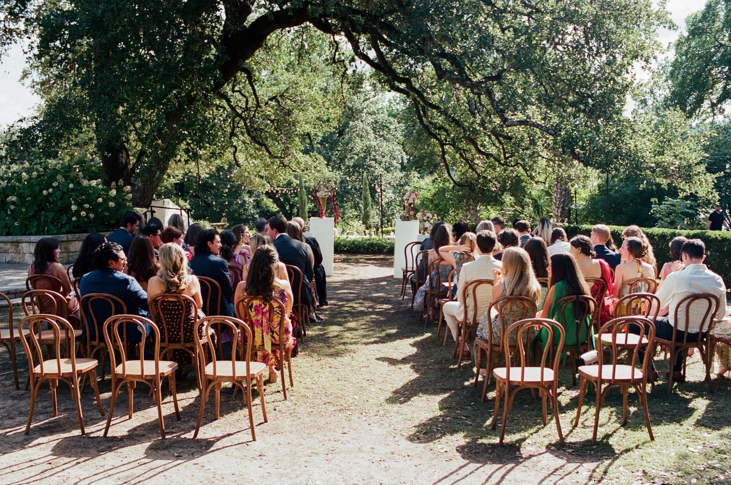 Rows of wooden chairs arranged outdoors under trees for a garden wedding ceremony.