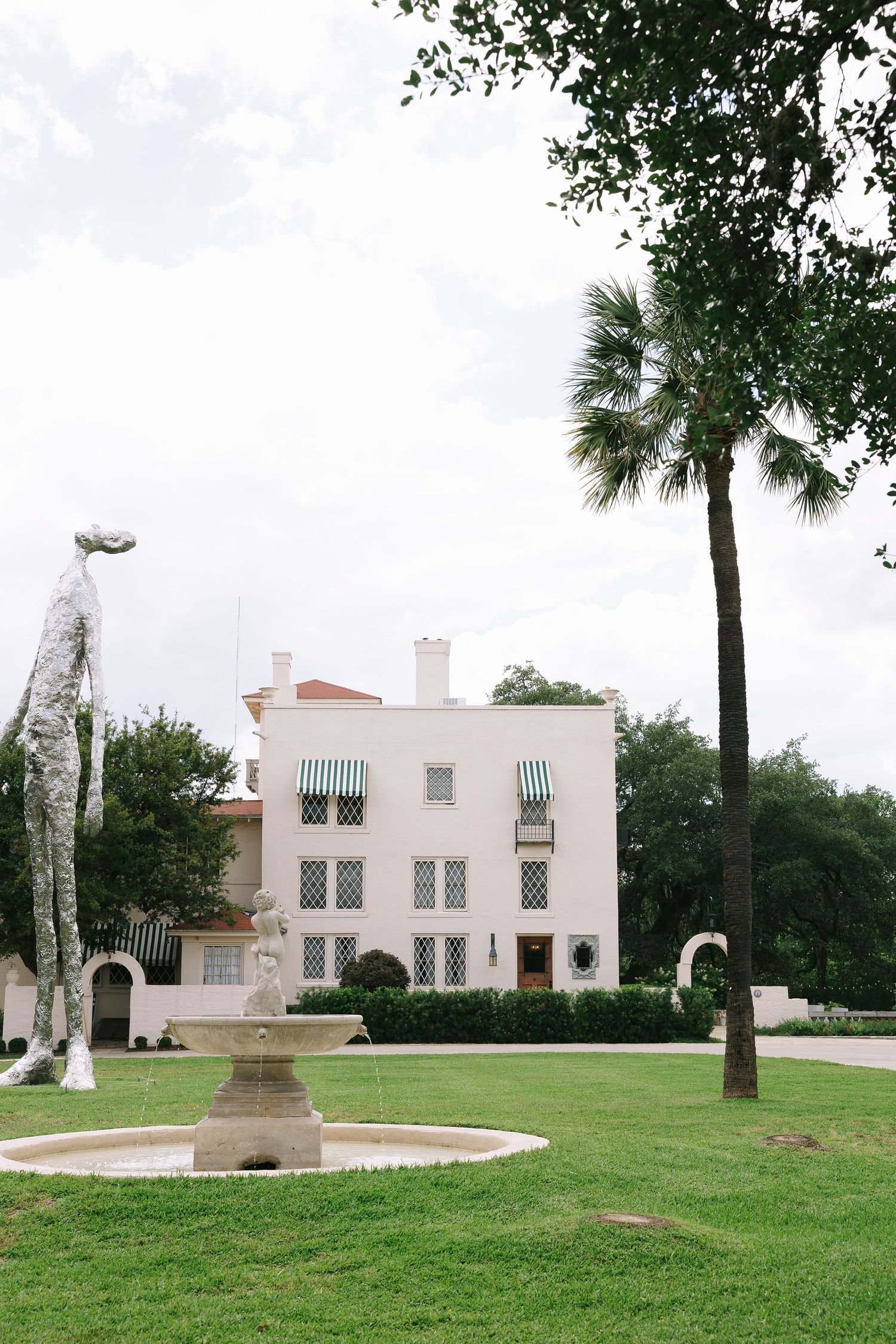 White Spanish-style buildings with green palm trees dot a manicured lawn on a sunny day.