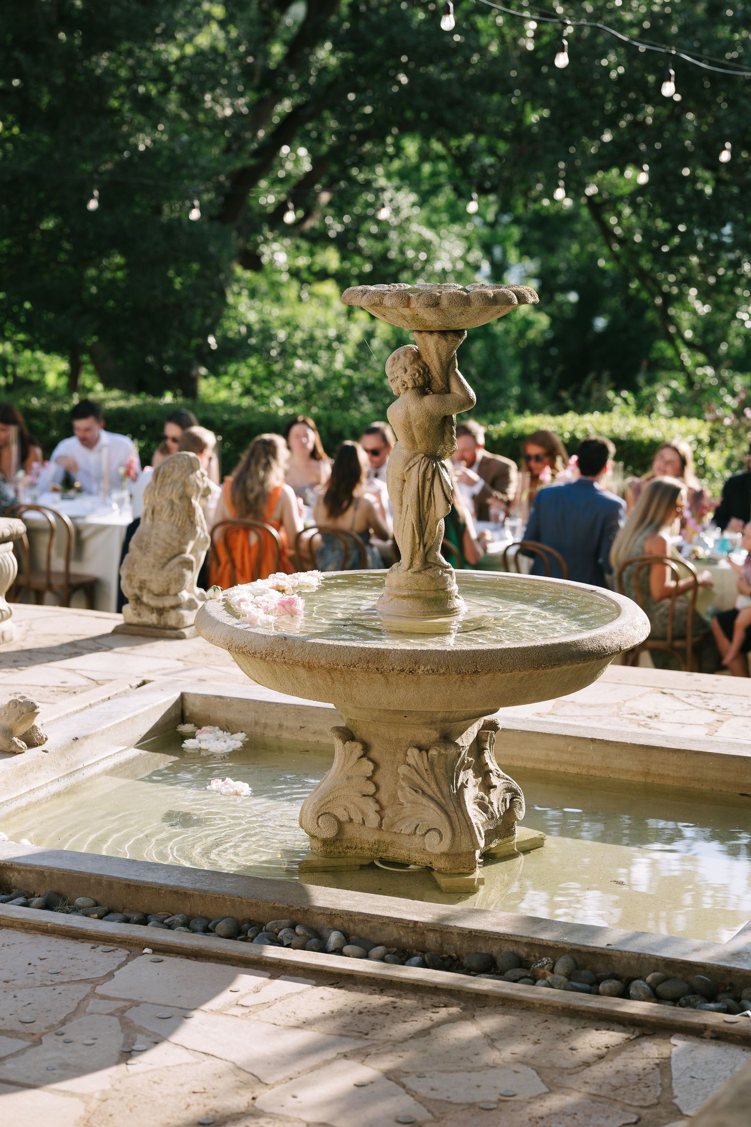 Ornate stone fountain with decorative details sits on a patio during an outdoor event.