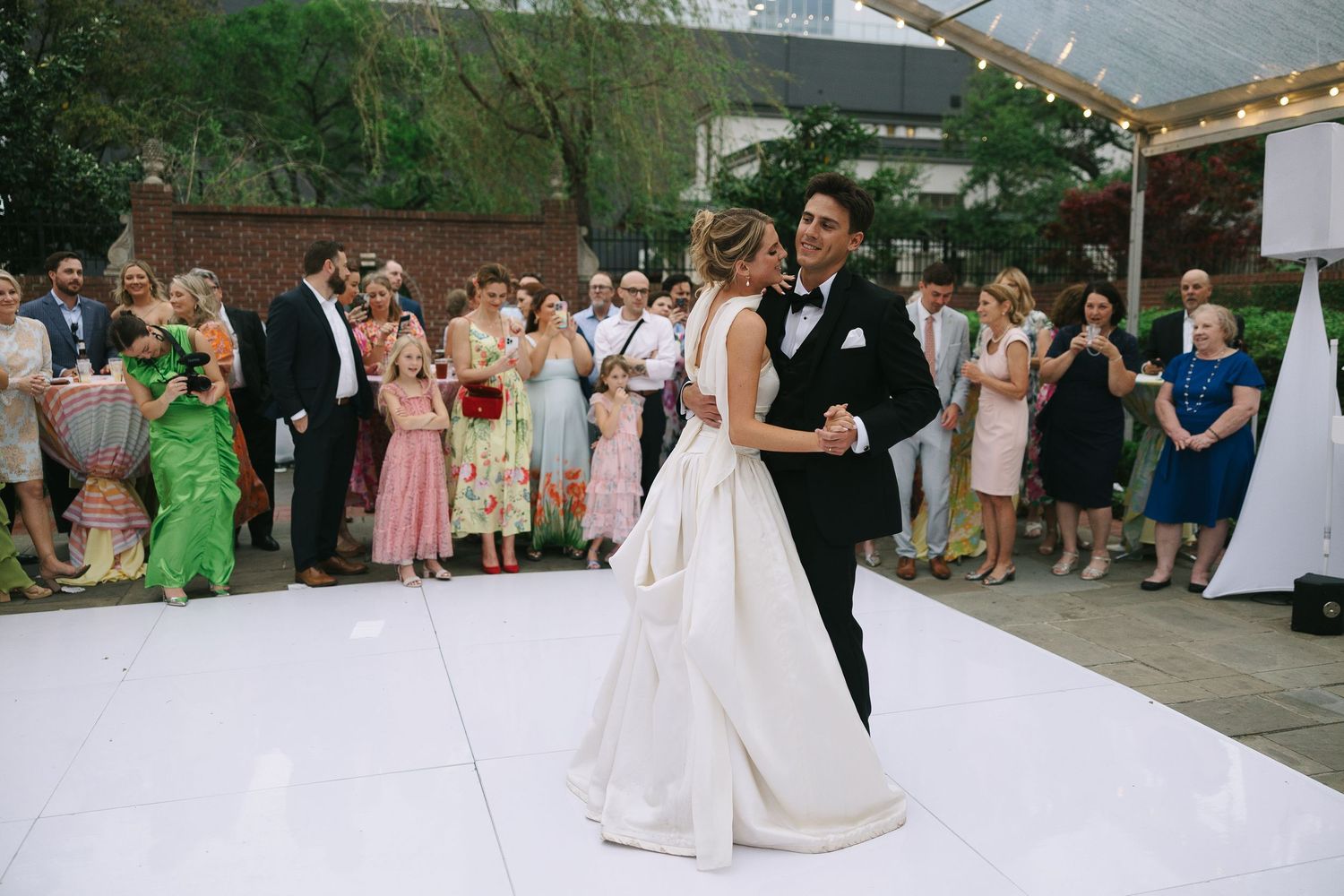 Wedding guests in colorful attire gather around the dance floor at an outdoor reception.