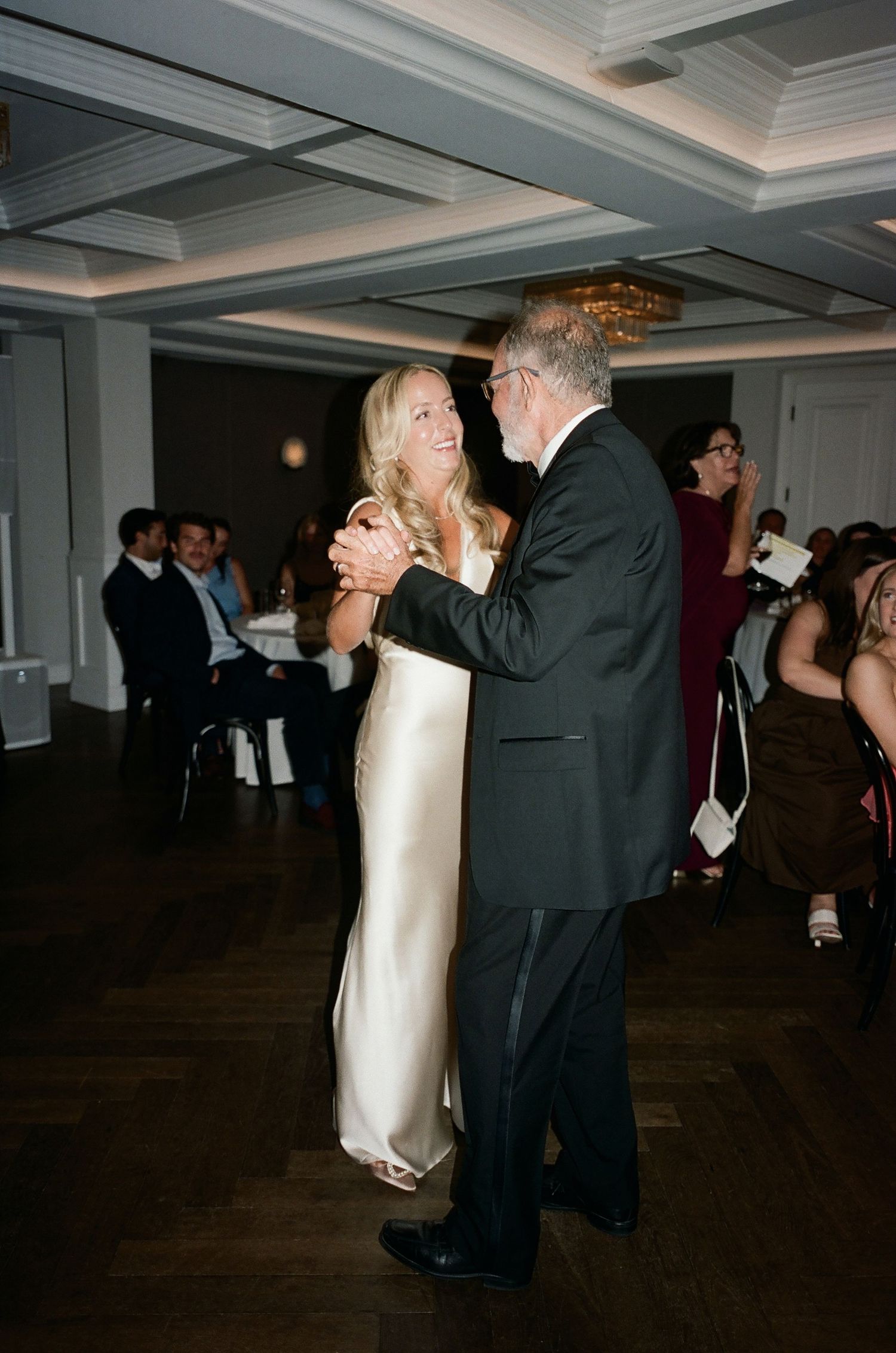 A couple shares a dance at a wedding reception in a ballroom with coffered ceilings.