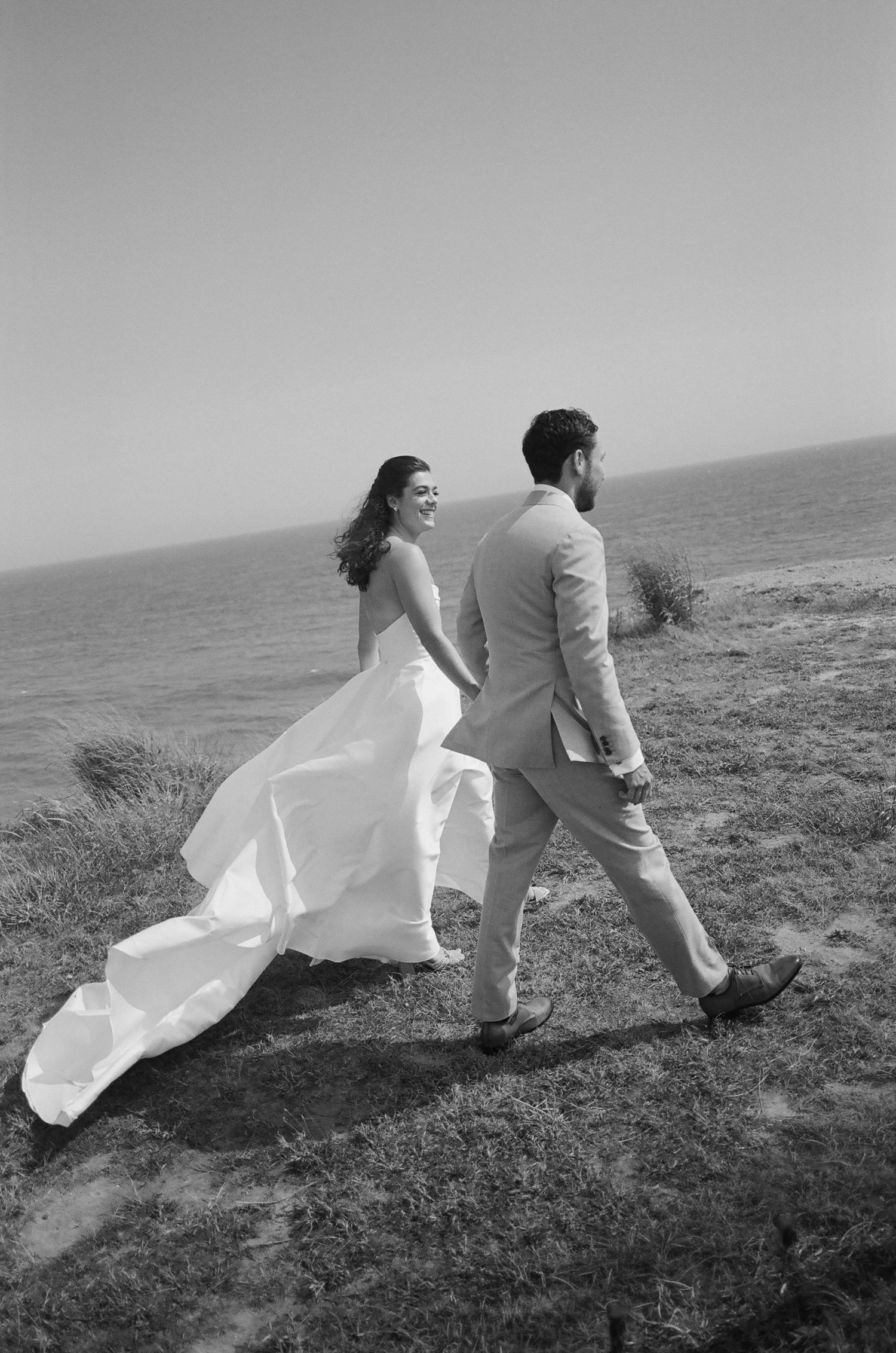 Black and white coastal photo with flowing white dress caught in ocean breeze.