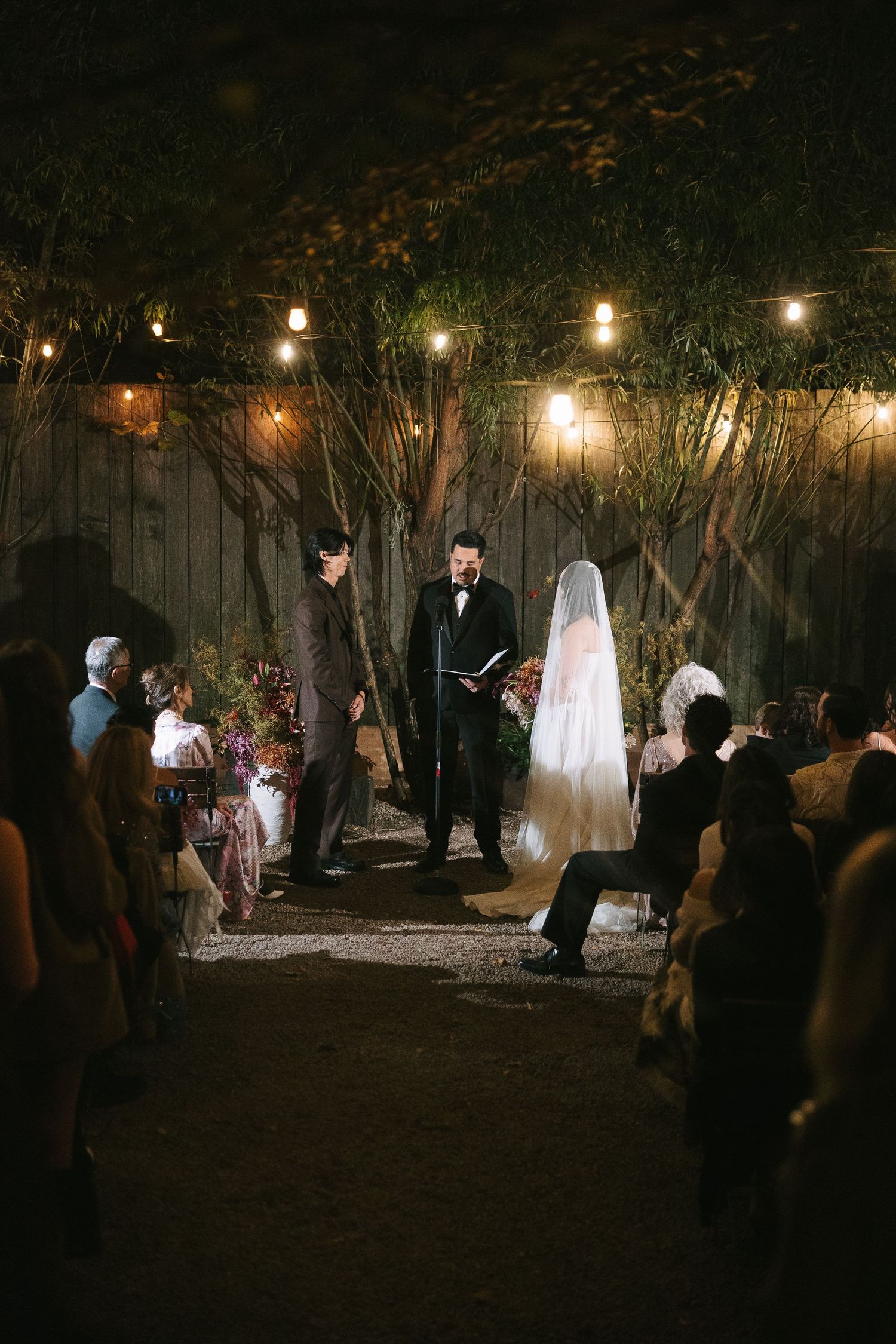 An outdoor nighttime wedding ceremony with string lights illuminating the garden setting.