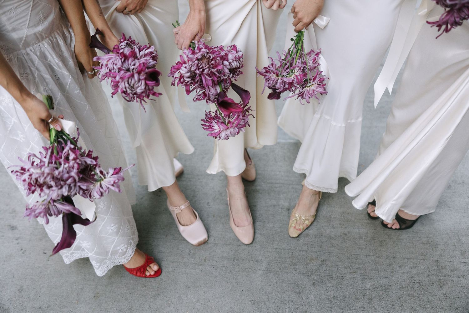 Close-up view of bridesmaids' feet showing various colorful shoes paired with white dresses.