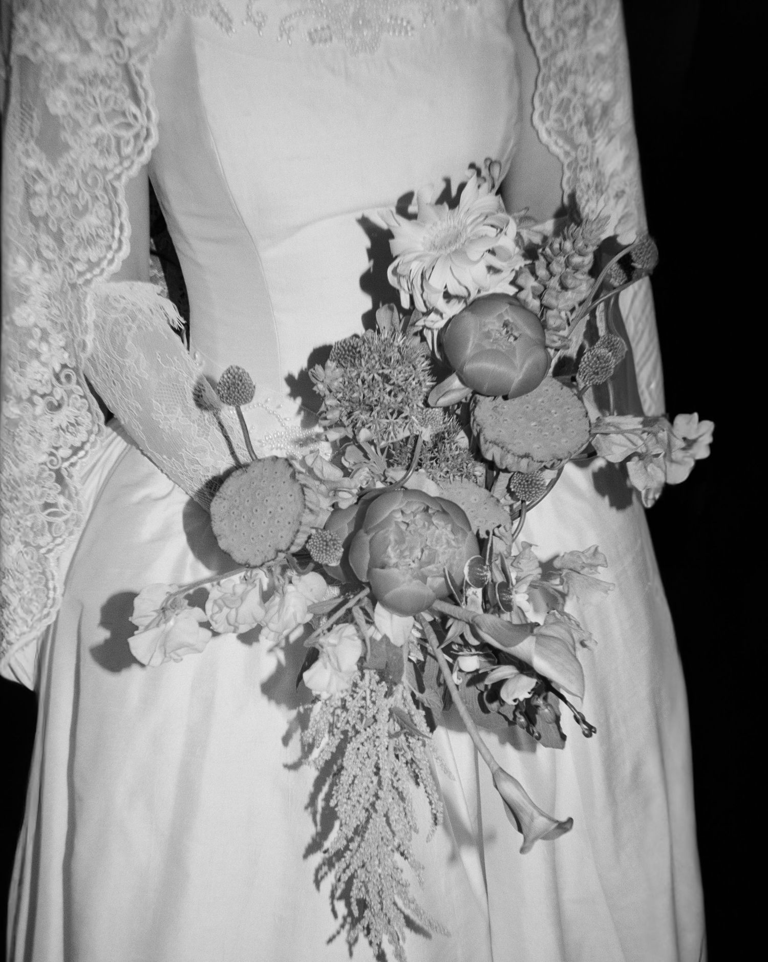 Bride in lace wedding gown holding cascading bouquet of roses and wildflowers in classic black and white photo.