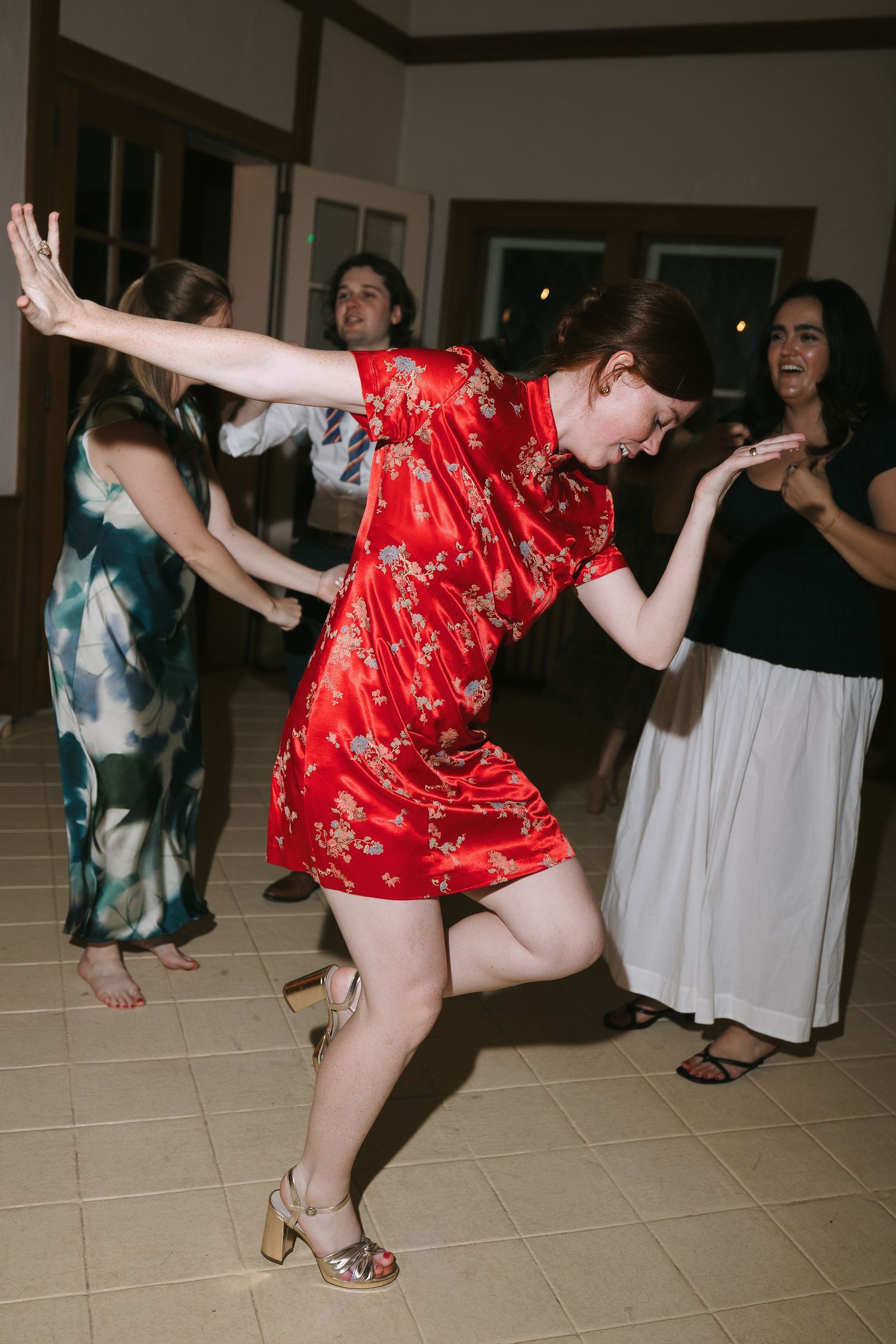 Guests dancing energetically at a wedding reception, with one person in a red patterned dress.
