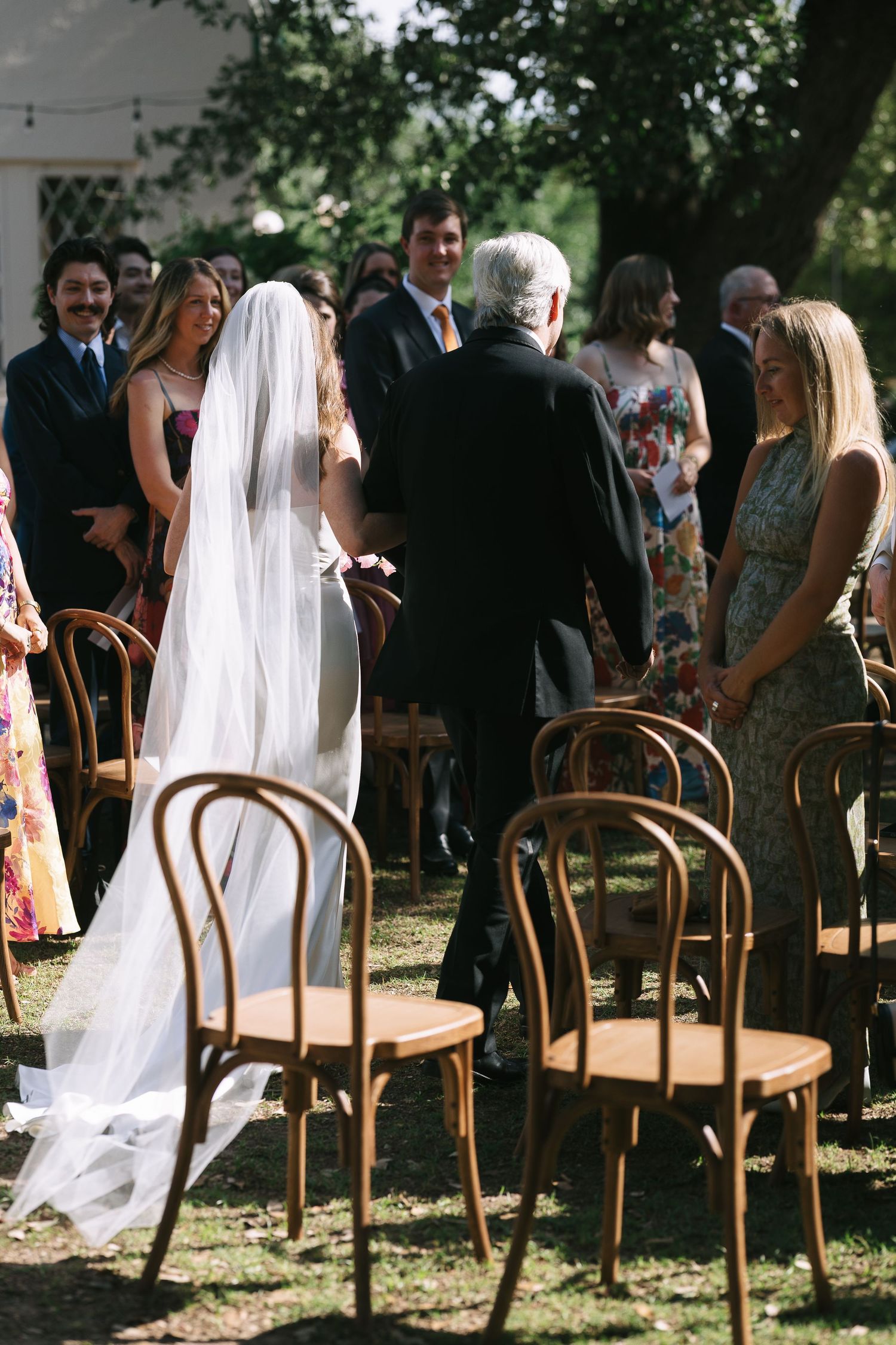Vintage wooden chairs arranged for outdoor wedding ceremony with flowing white veil in view.