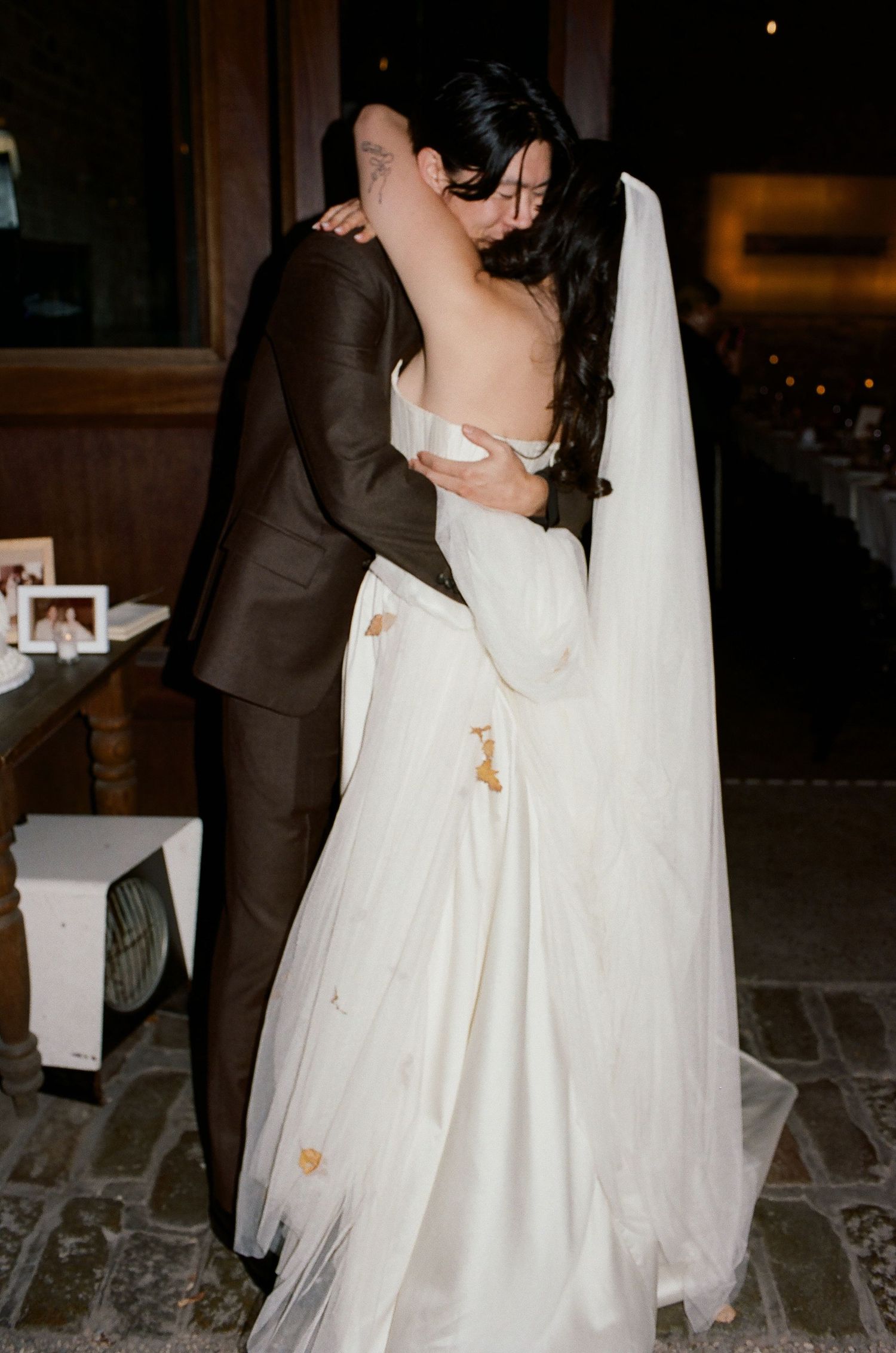 A couple in wedding attire dance together on a stone floor during their first dance at an evening reception.