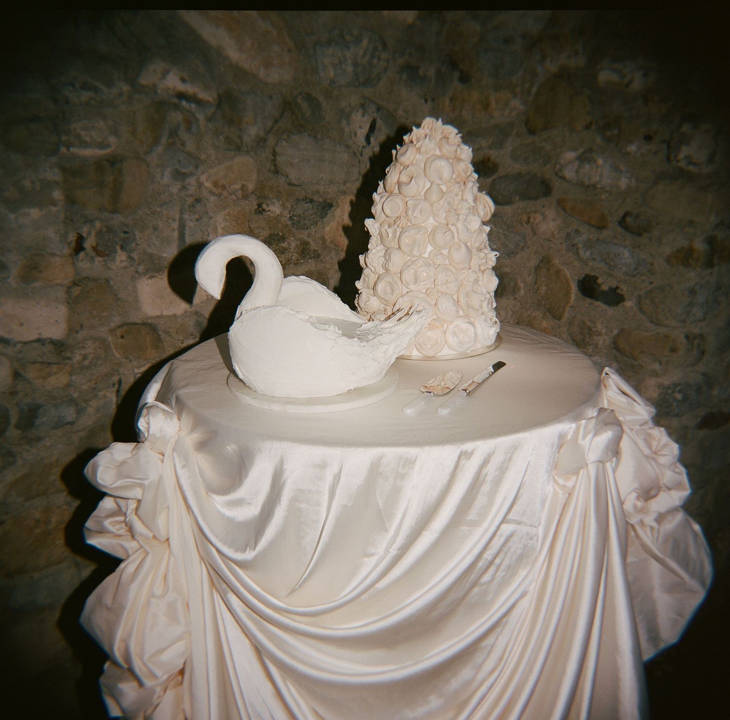 Elegant white swan figurine with floral arrangement centerpiece on satin-draped pedestal table against stone wall.