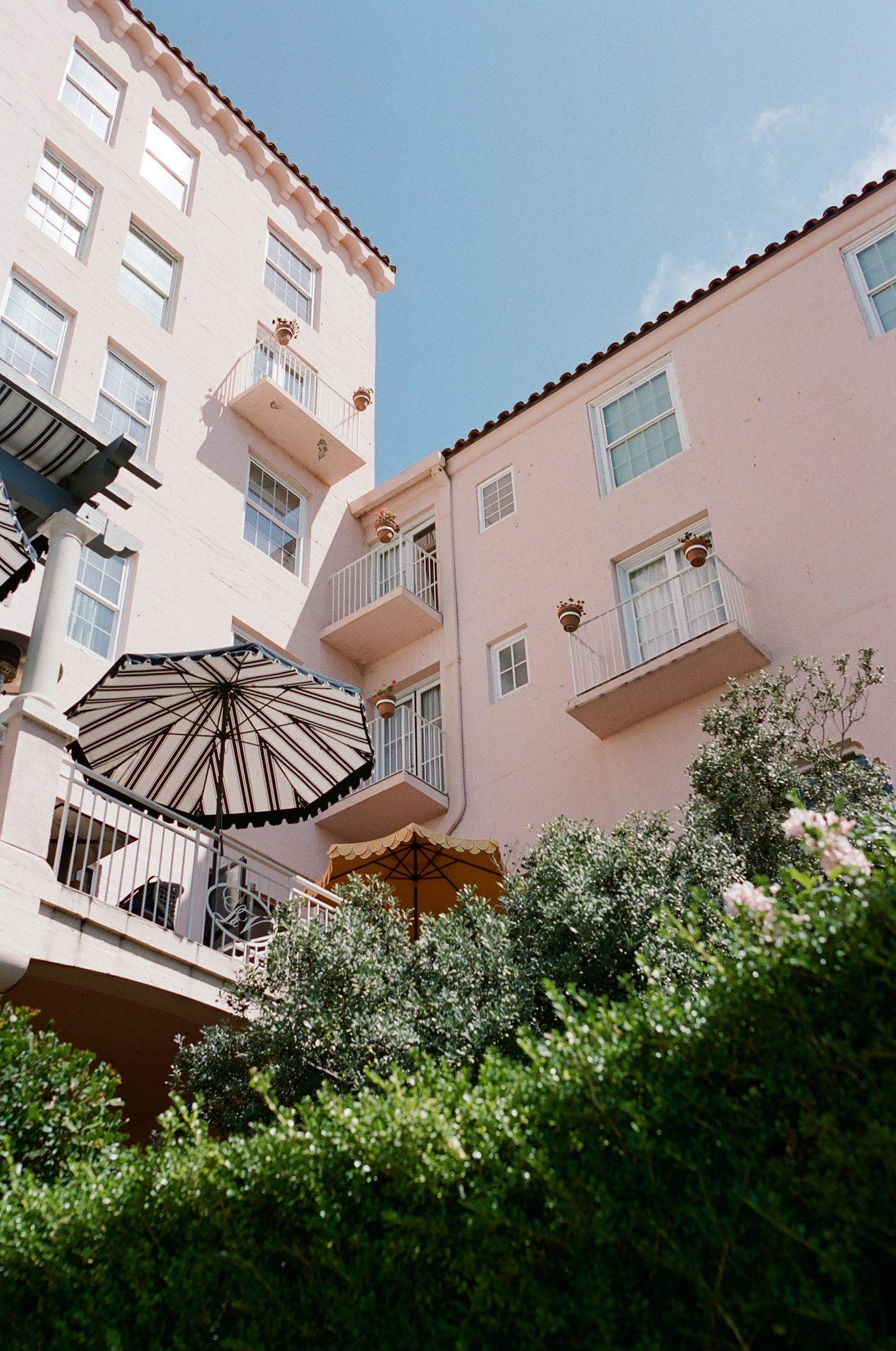 Pink stucco building with white balconies and black striped awnings against blue sky.