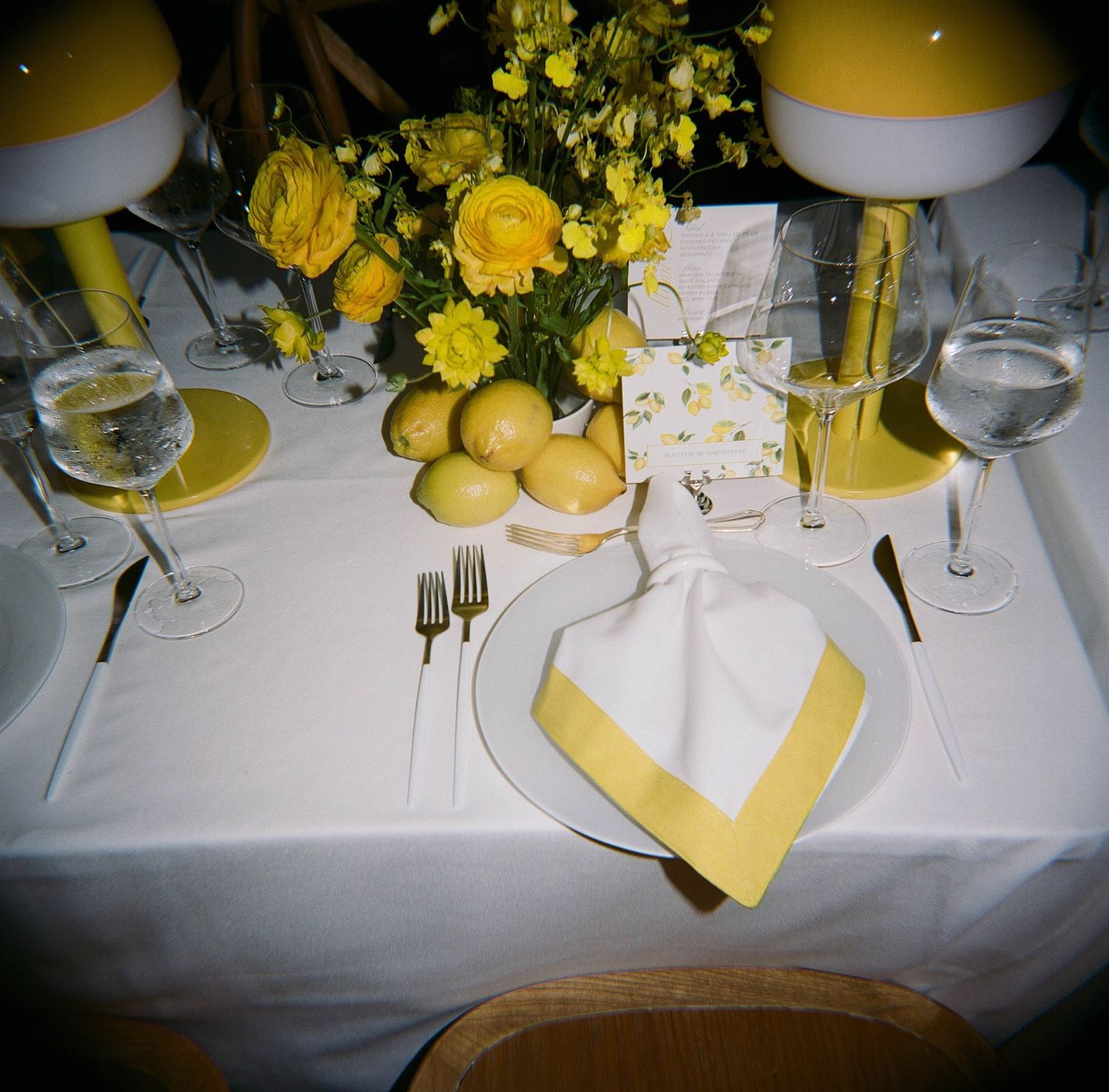 Wedding table setting with yellow floral centerpieces and white linens.