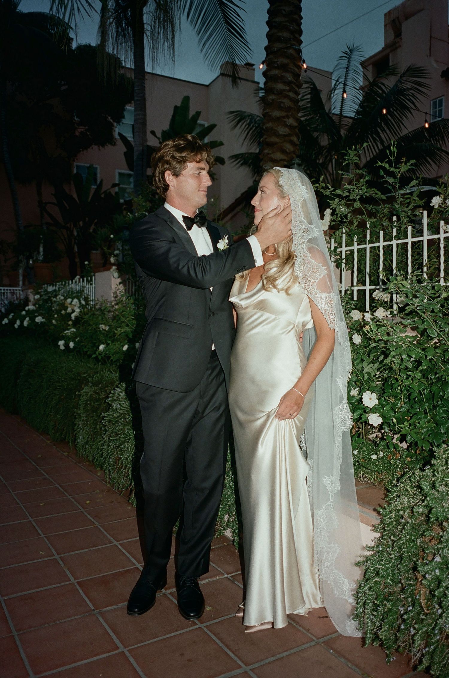 Evening wedding portrait in a garden setting with palm trees and white flowers.
