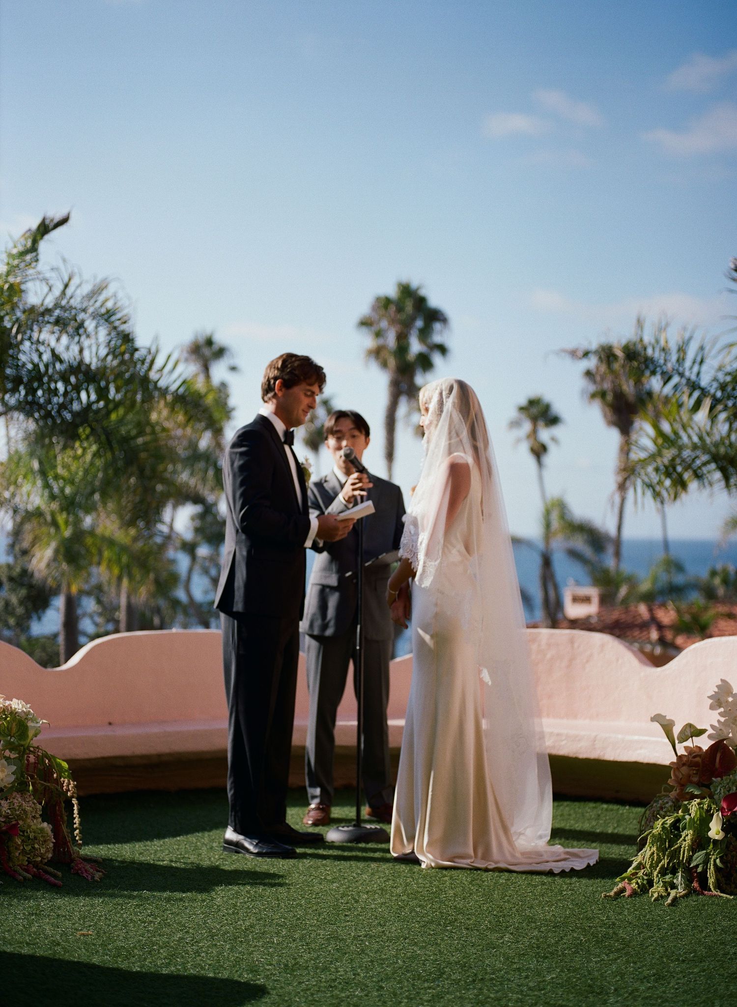 Wedding ceremony on a rooftop terrace with palm trees and ocean views.
