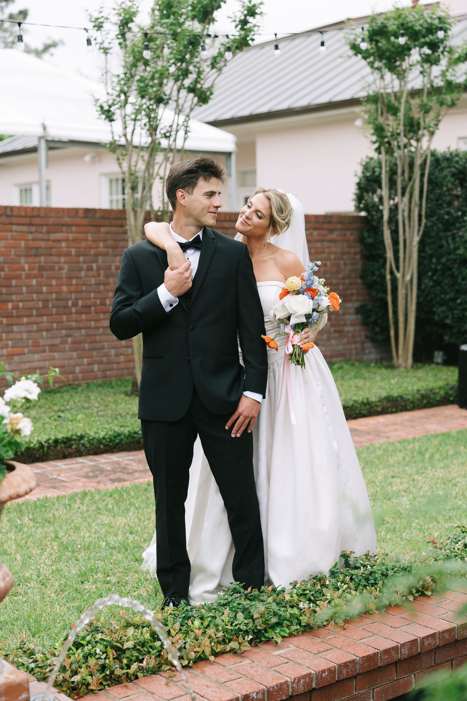 A couple shares joyful moments during their wedding photoshoot in a garden with brick walls.