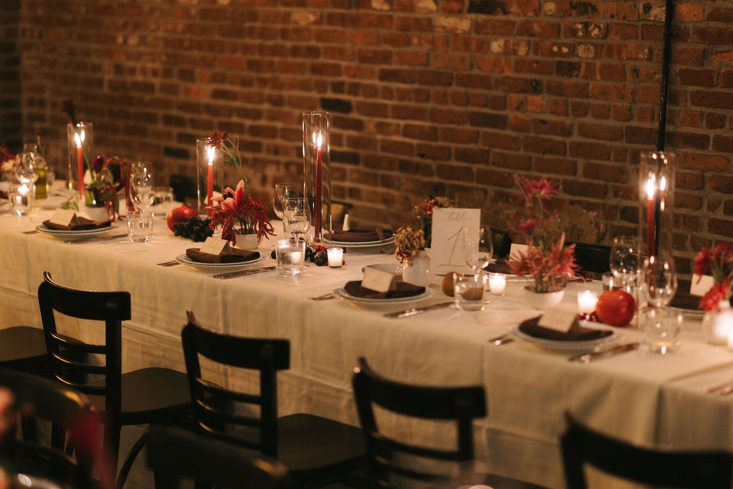 Intimate wedding reception setup with dark wooden chairs and brick walls lit by candlelight.