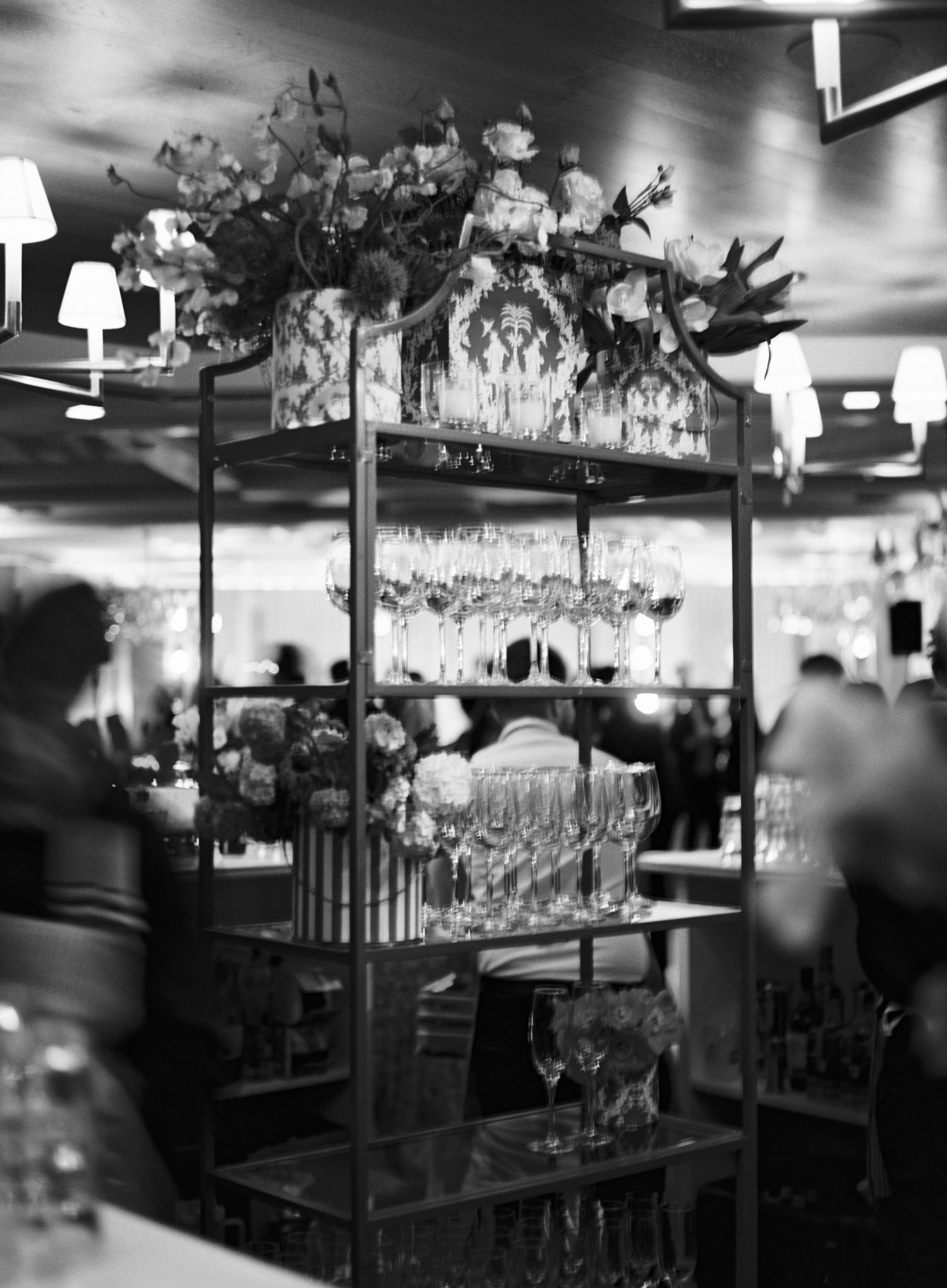 Black and white image of elegant wine glasses displayed in a bar setting with dramatic lighting.