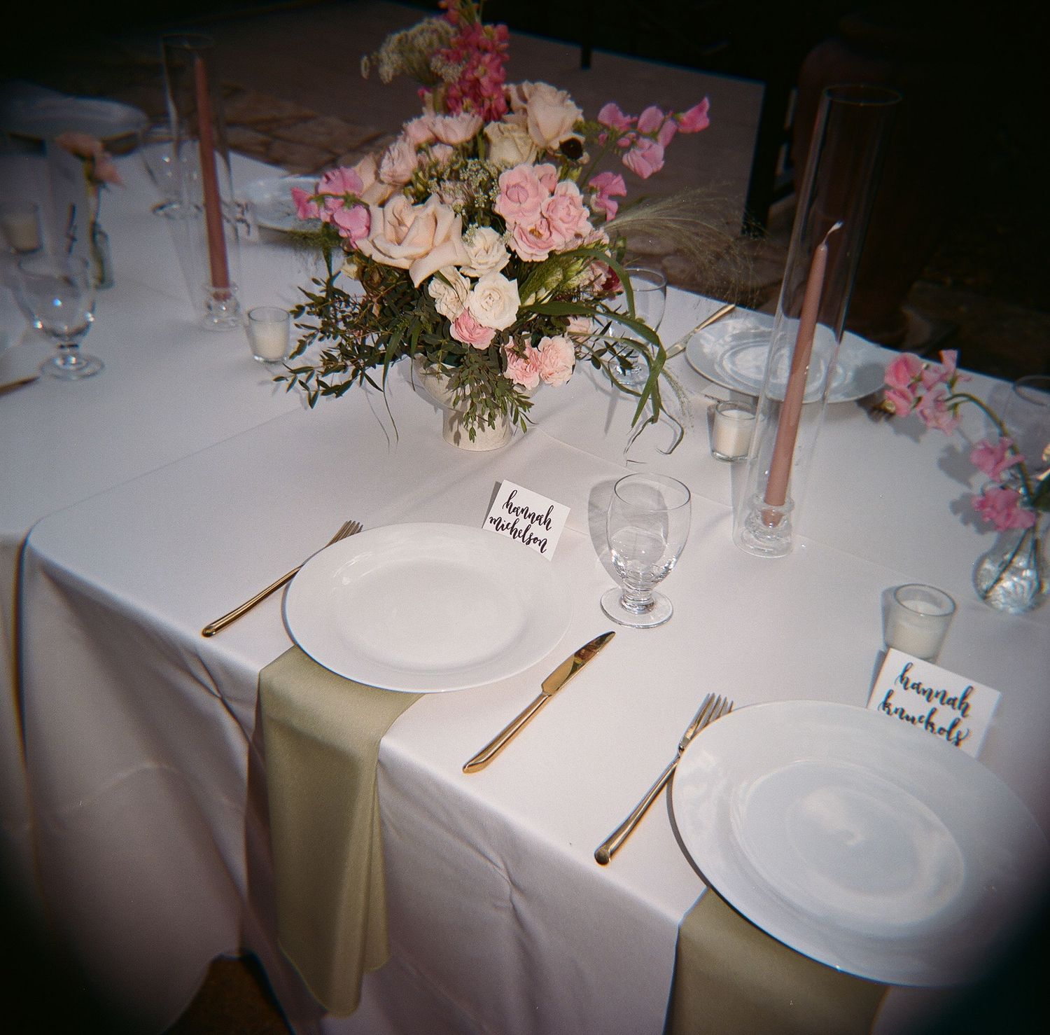 Elegant table setting with pink floral centerpiece, white plates and rose gold cutlery.