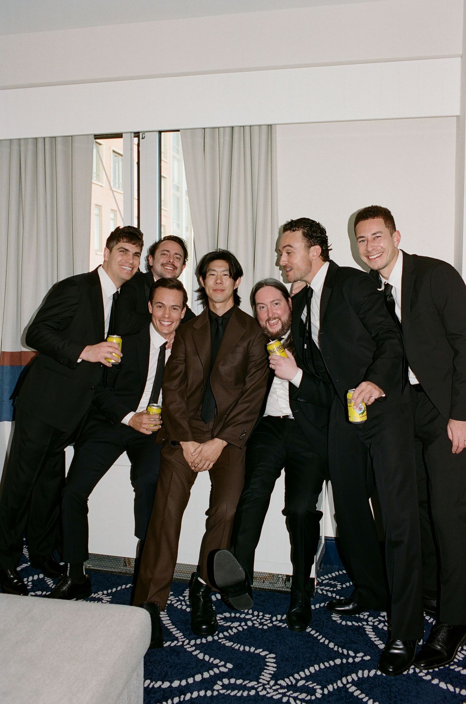 A group of men in formal attire pose together on a patterned carpet in what appears to be a hotel room.