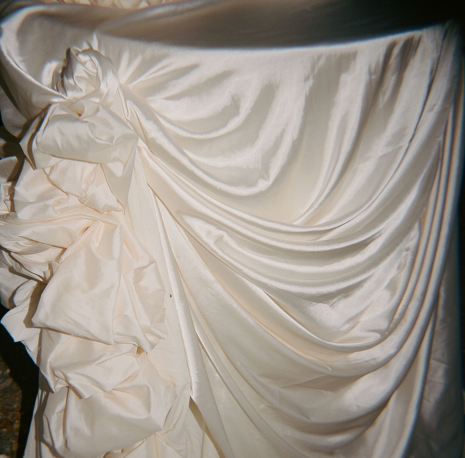 Elegant ivory white wedding dress fabric with luxurious draped satin folds and ruffled details.