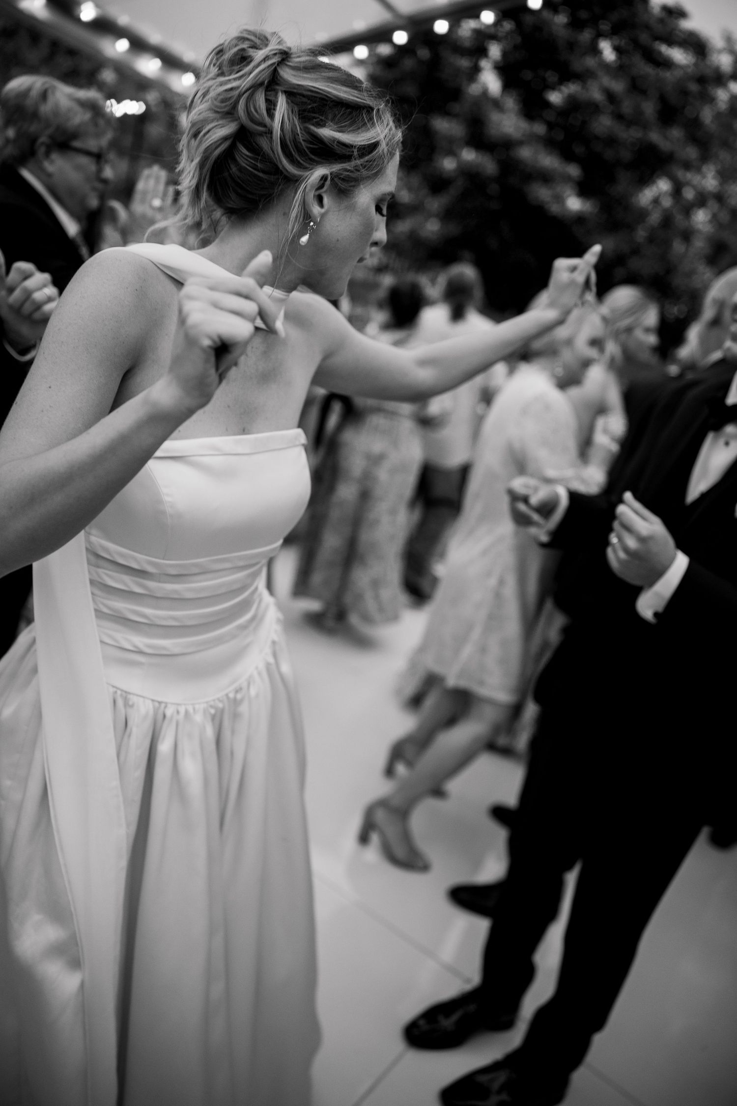 Black and white photo of wedding guests dancing in formal attire.