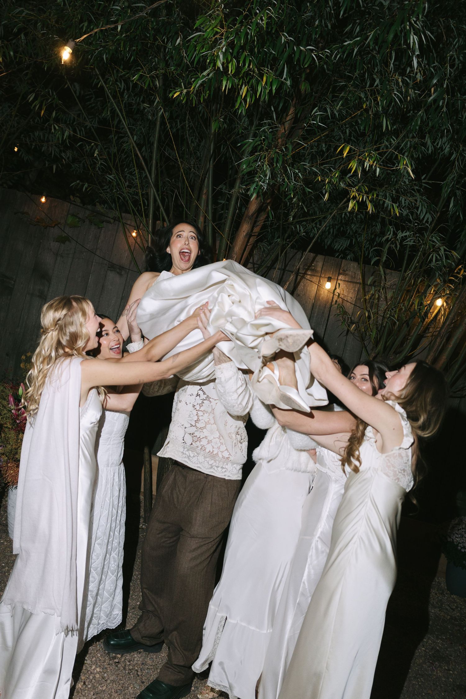Party guests in white clothing form a playful dance line outdoors at night.
