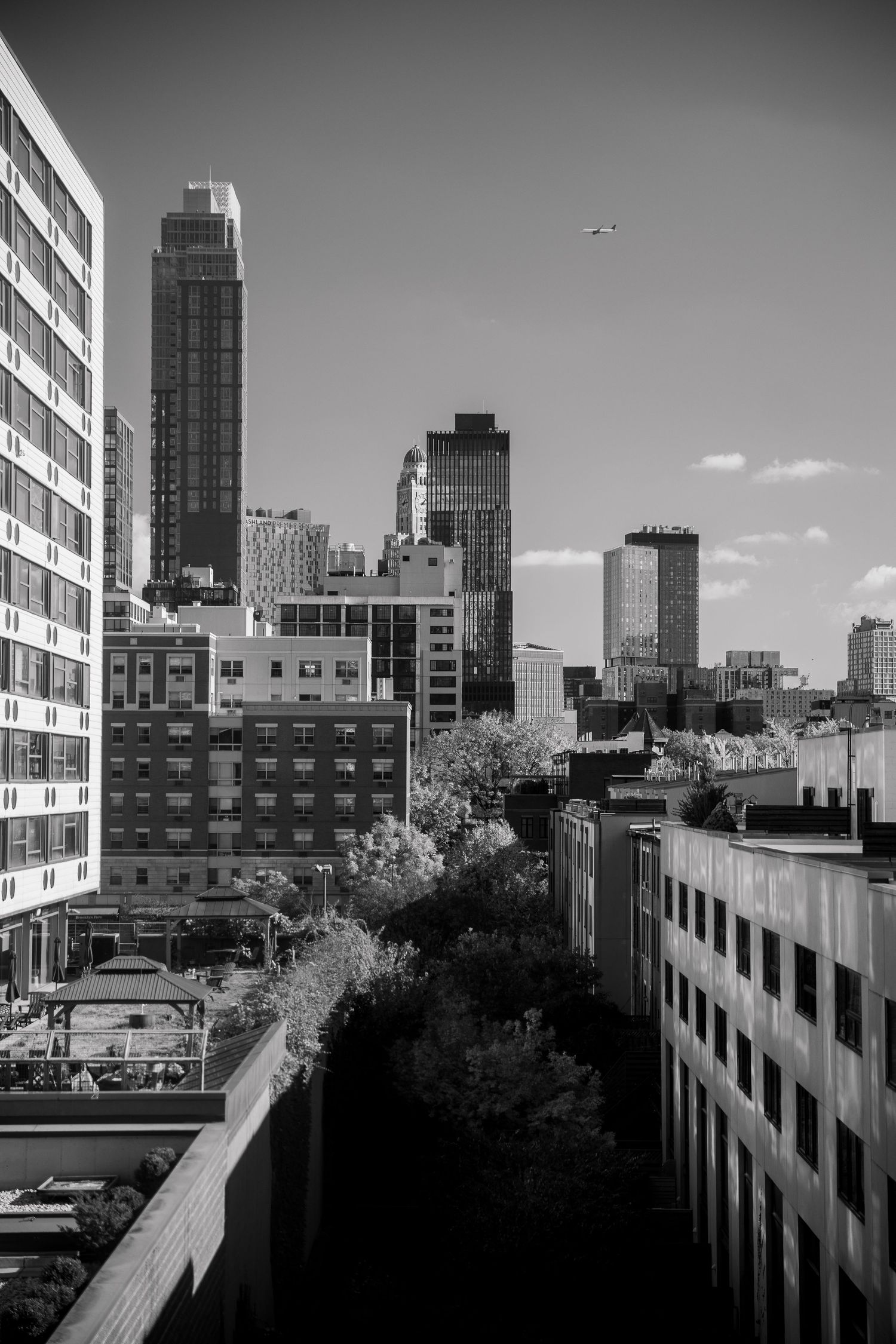 Black and white cityscape showing urban buildings and skyscrapers against a cloudy sky.