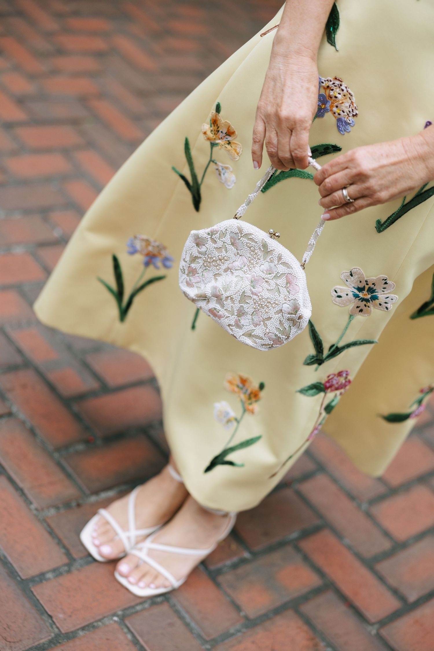 Yellow floral dress detail with lace handkerchief on brick pavement.