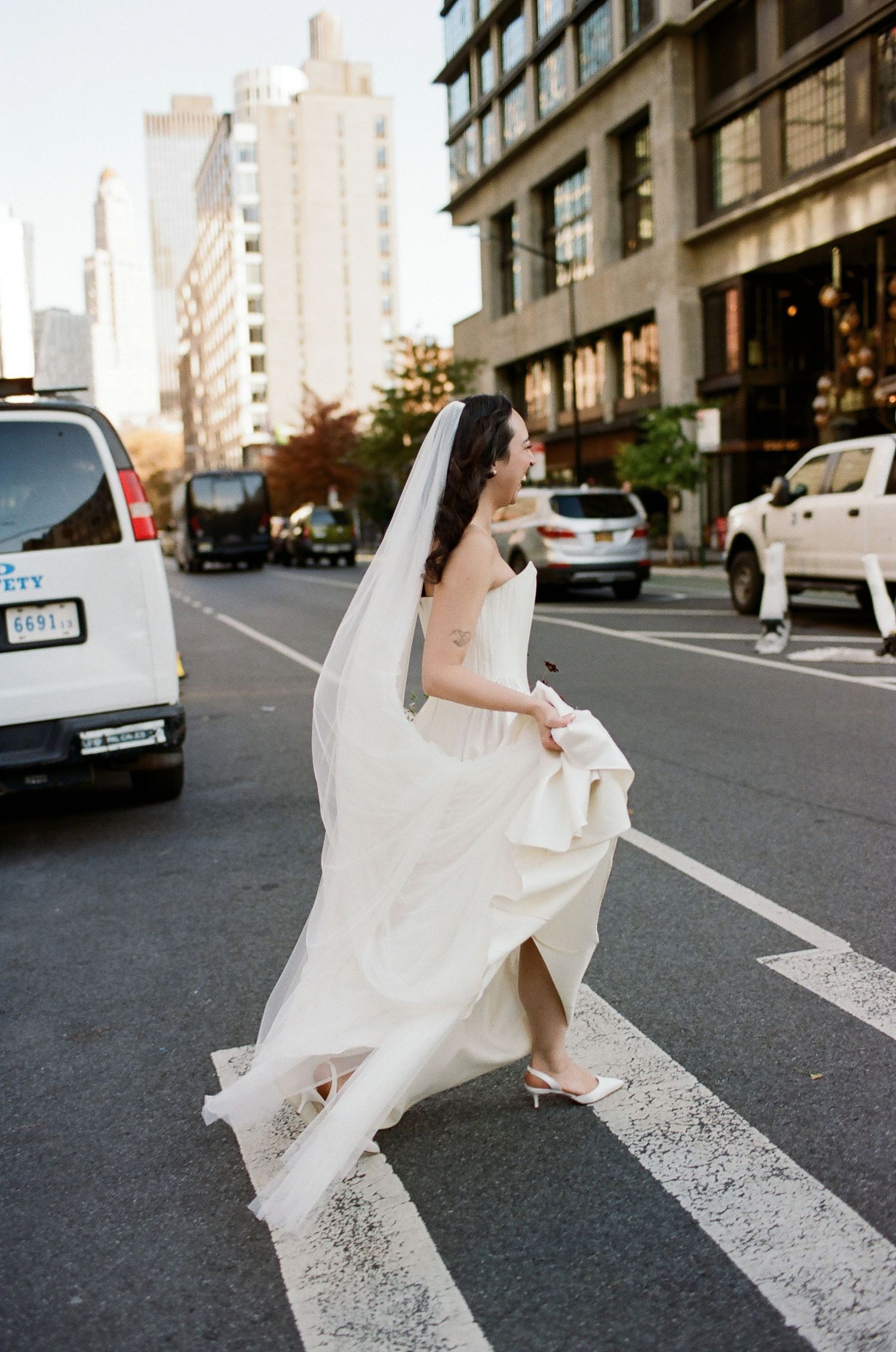 A woman in a flowing white dress dances gracefully across a city crosswalk in a sequence of motion photographs.