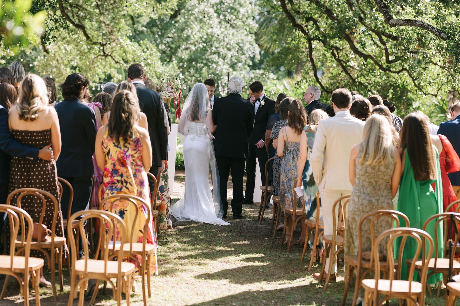 Wedding guests seated in wooden chairs during an outdoor garden ceremony.