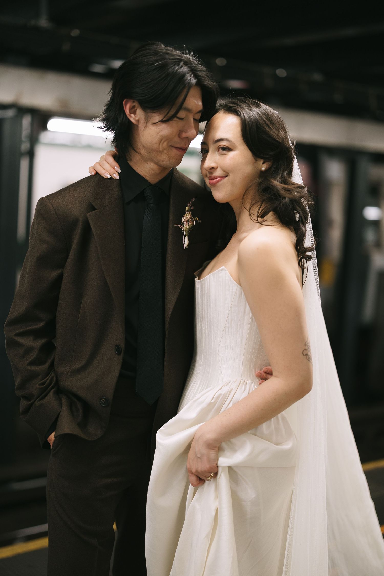 Newlyweds share tender moments in dark indoor setting wearing formal attire.