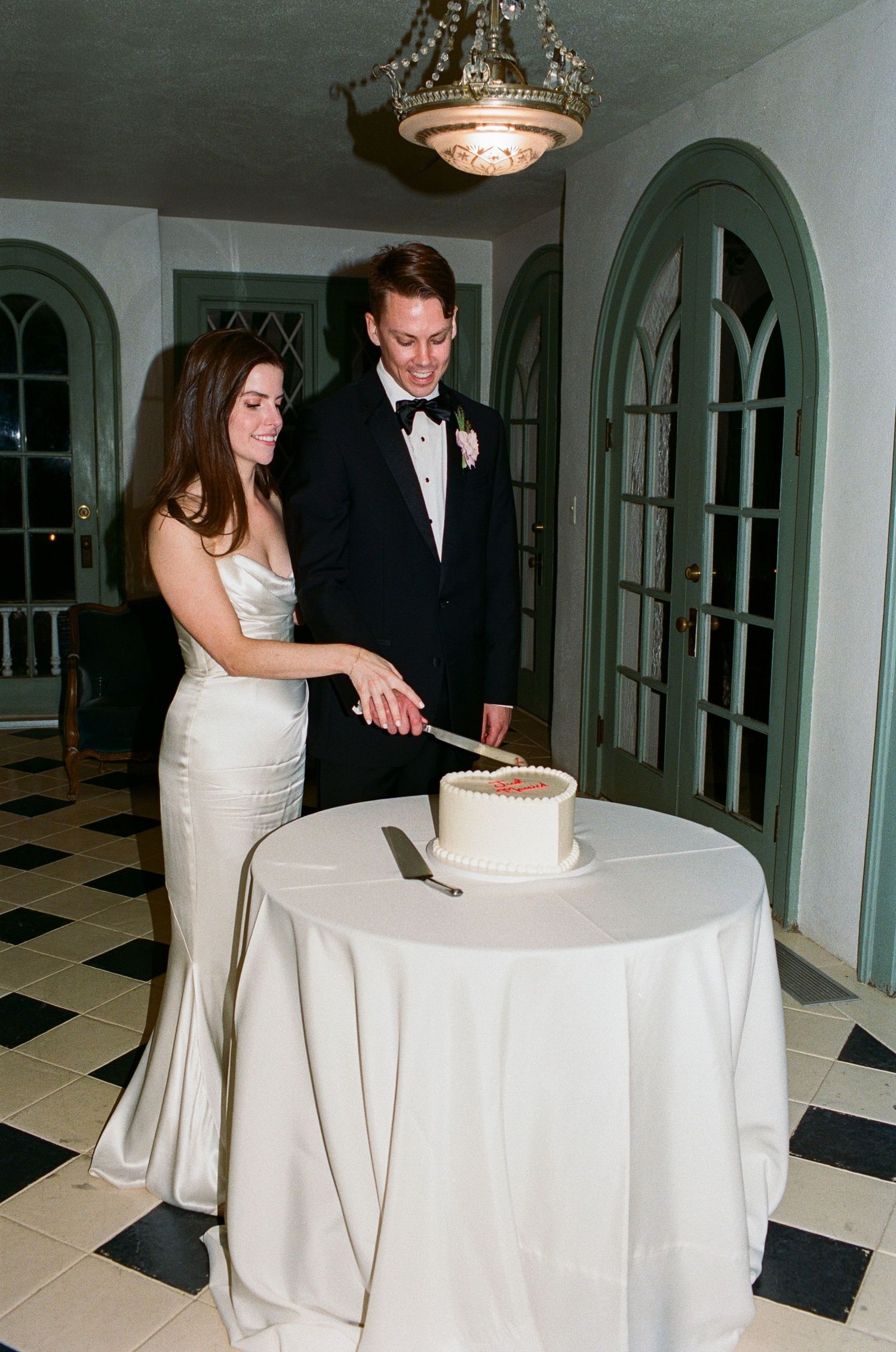 Couple cutting their wedding cake together at a reception with black and white checkered floor.