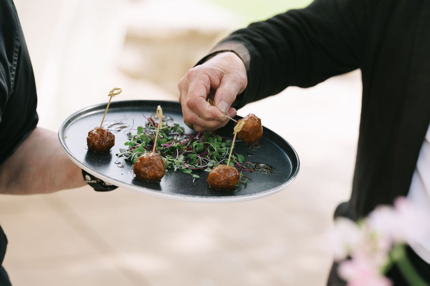 Hands reaching for appetizers on black plates at a catered event.
